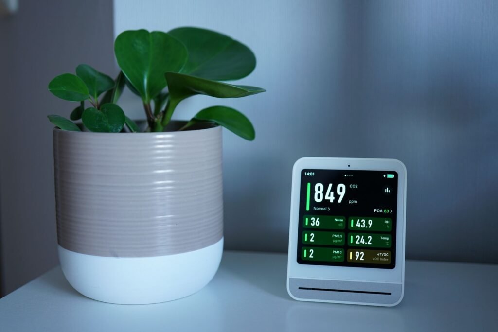 Indoor air quality monitor showing humidity and temperature beside a houseplant