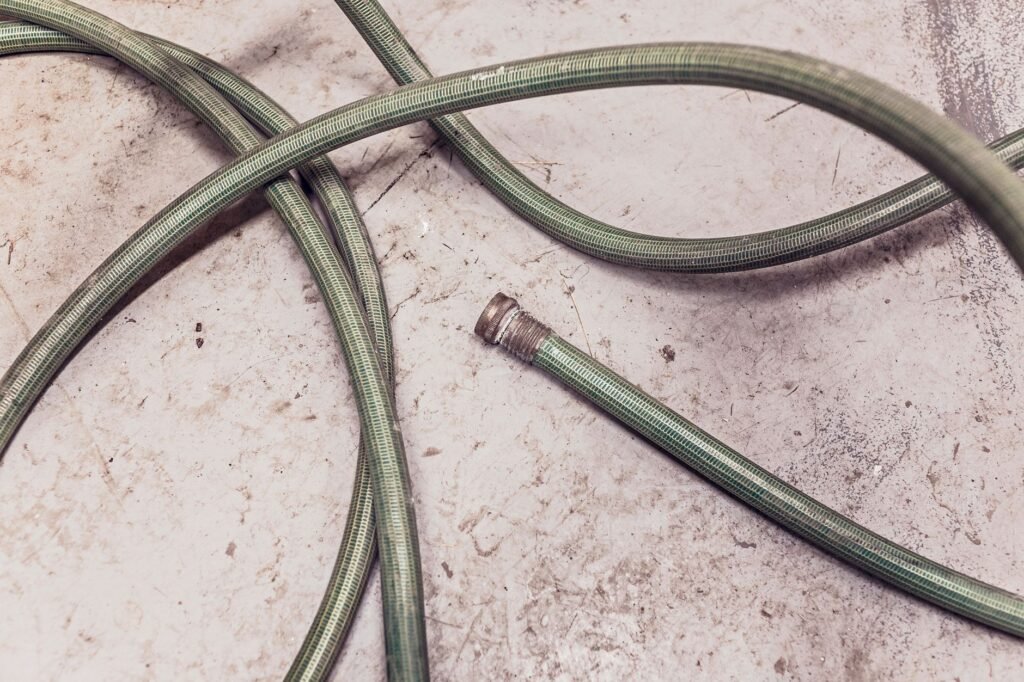 Coiled garden hose with a threaded fitting on a concrete floor, the type used for dehumidifier drainage