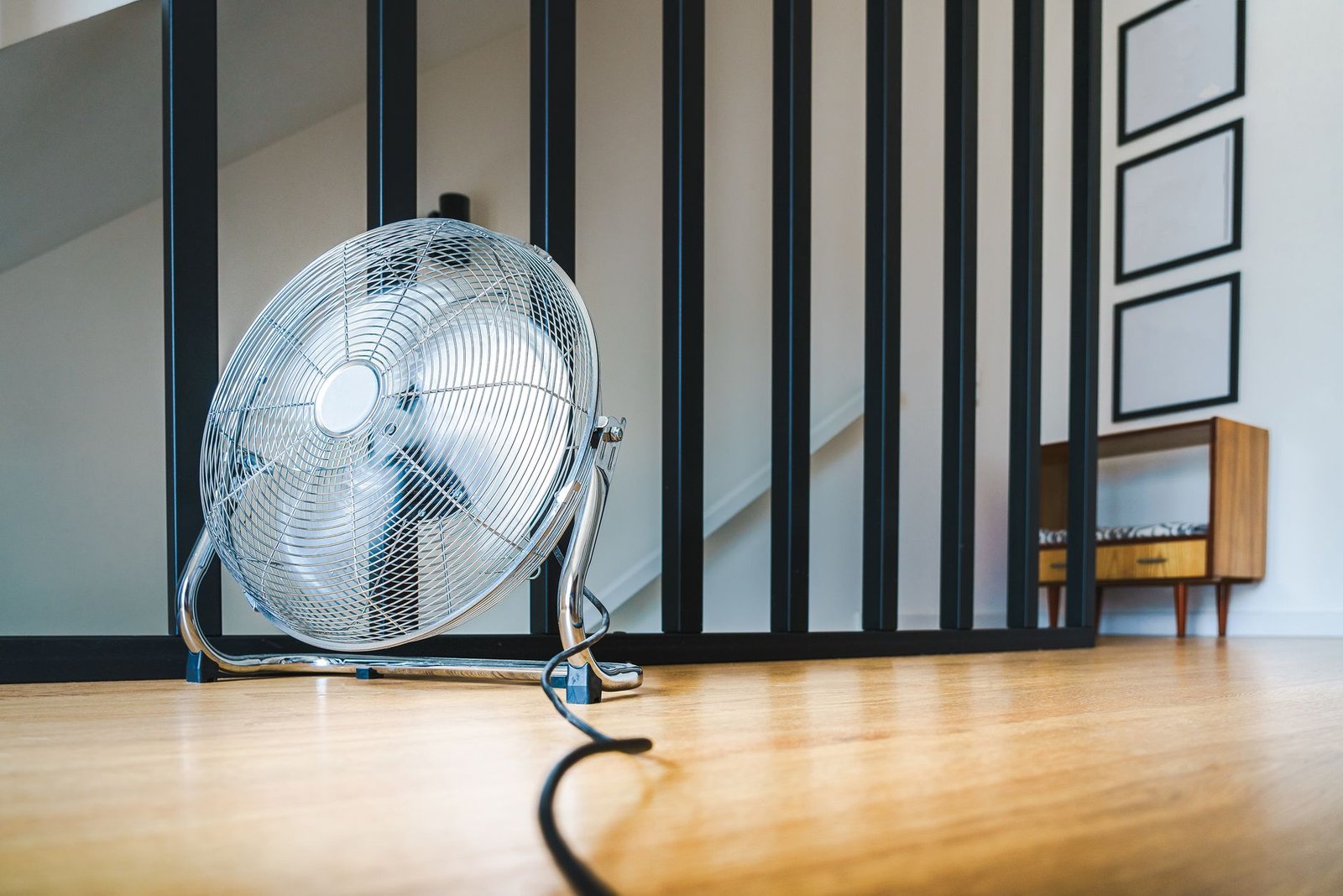 Chrome electric floor fan running in a warm hallway, the usual first attempt at cooling a room