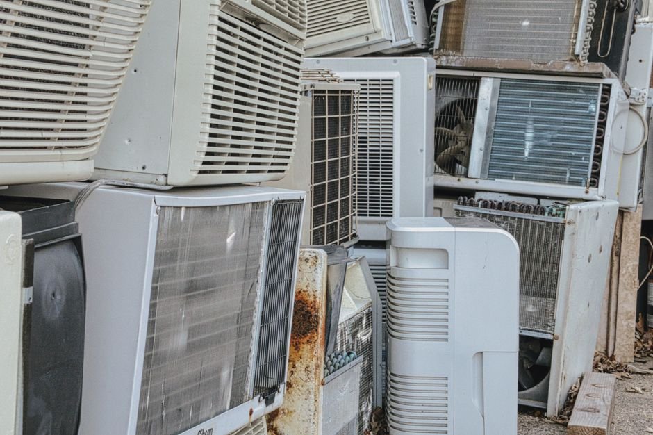 A pile of scrapped air conditioning and refrigeration units showing rusted coils and grilles, the end point for compressor appliances after five to ten years
