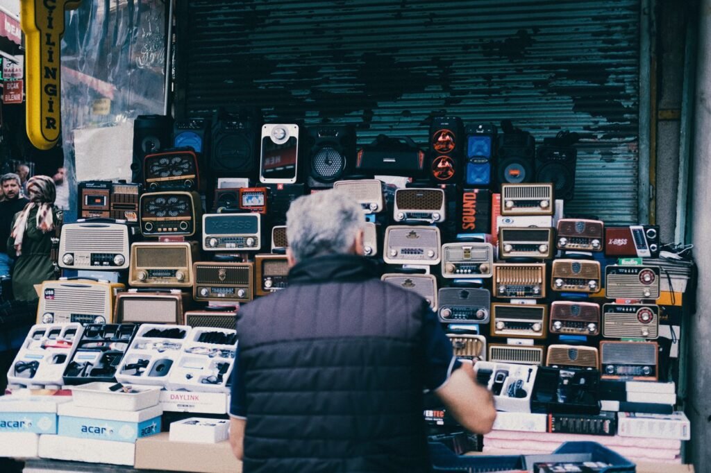 Second-hand electronics and radios stacked on a market stall, where used appliances change hands