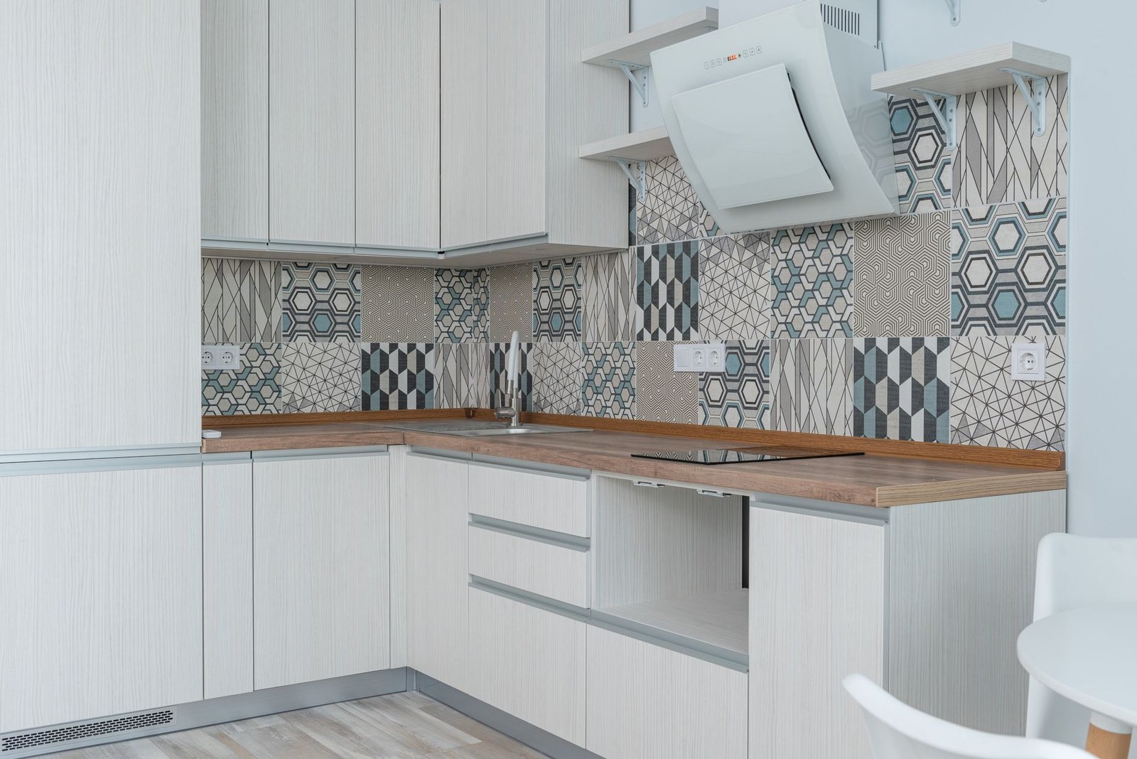 Angled white cooker hood on the wall of a kitchen with a patterned tile splashback