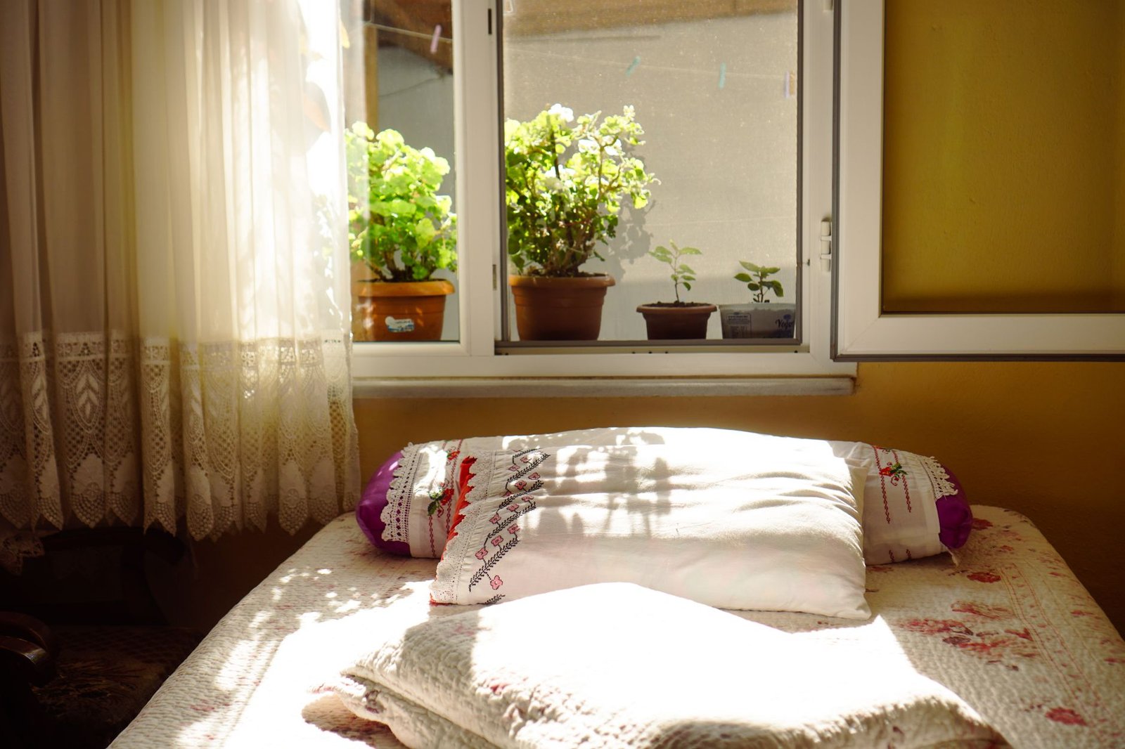 Sunlit bedroom with the casement window open and a net curtain drawn back, airing the room