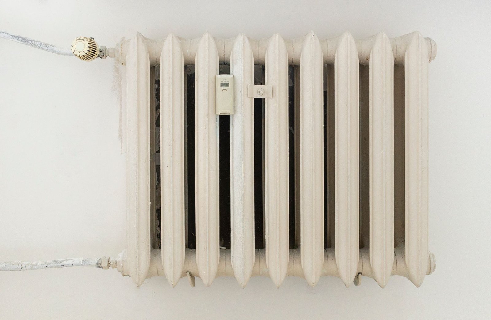 Cream cast-iron radiator on a plain wall, the kind of heat source people pair with a dehumidifier in a cold room