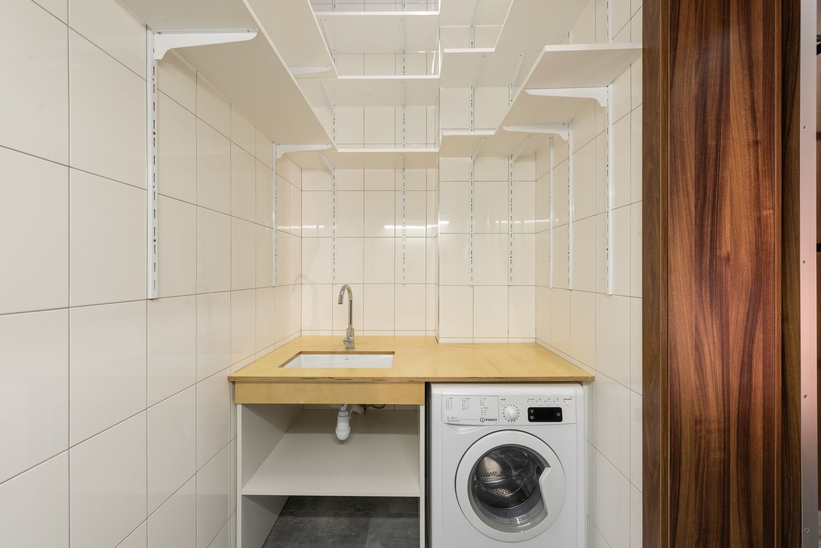 Compact tiled utility room with a washing machine under a worktop and sink, with the door open to the hall