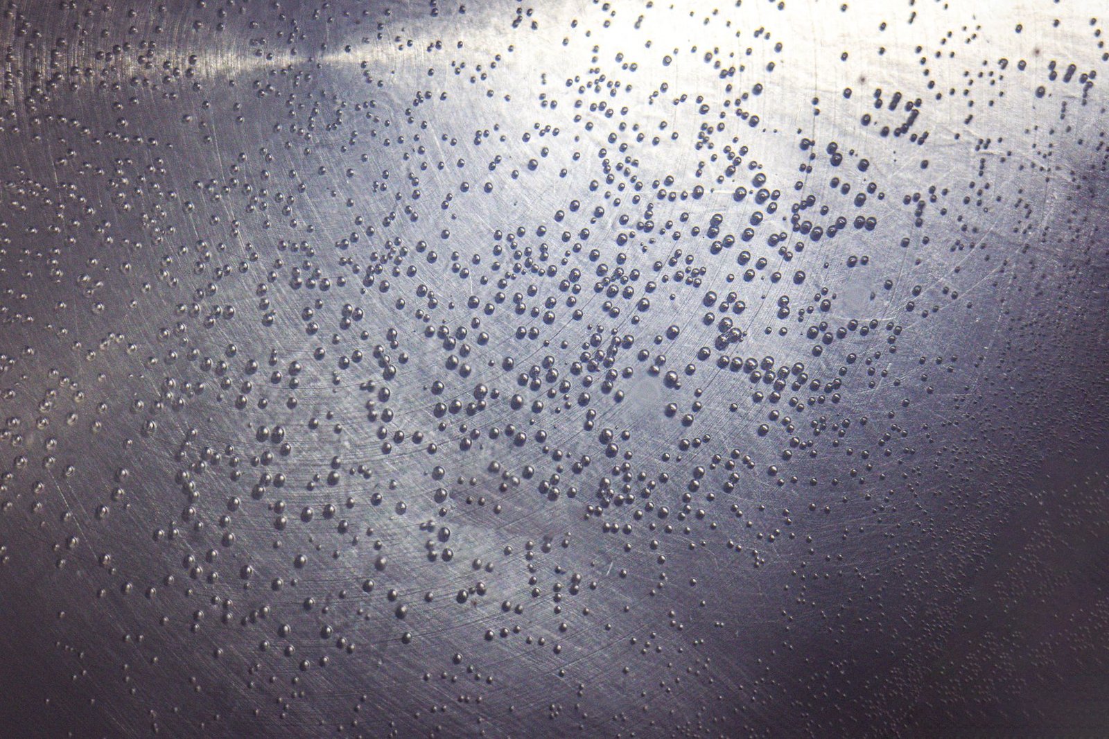Small water droplets condensed on a brushed metal surface, the same effect a cold dehumidifier coil produces