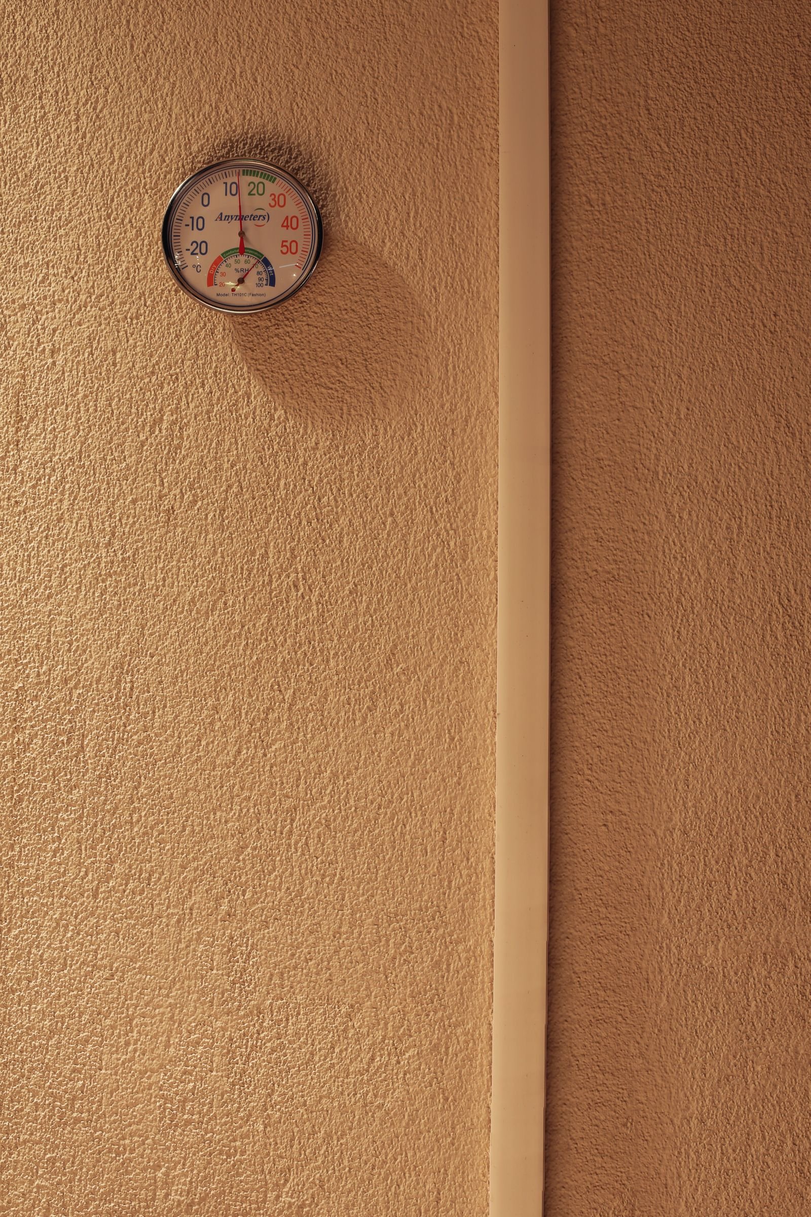 Round dial thermometer and hygrometer mounted on a textured plaster wall
