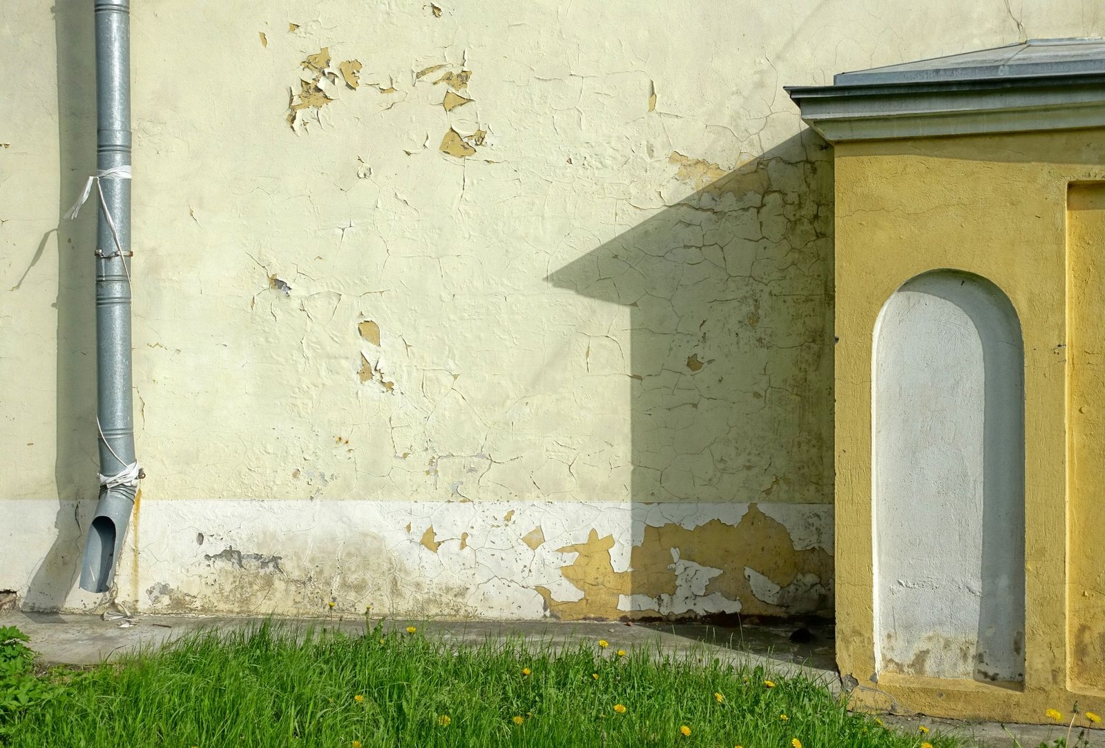 Exterior wall with a metal downpipe and paint peeling off at the damp base of the wall