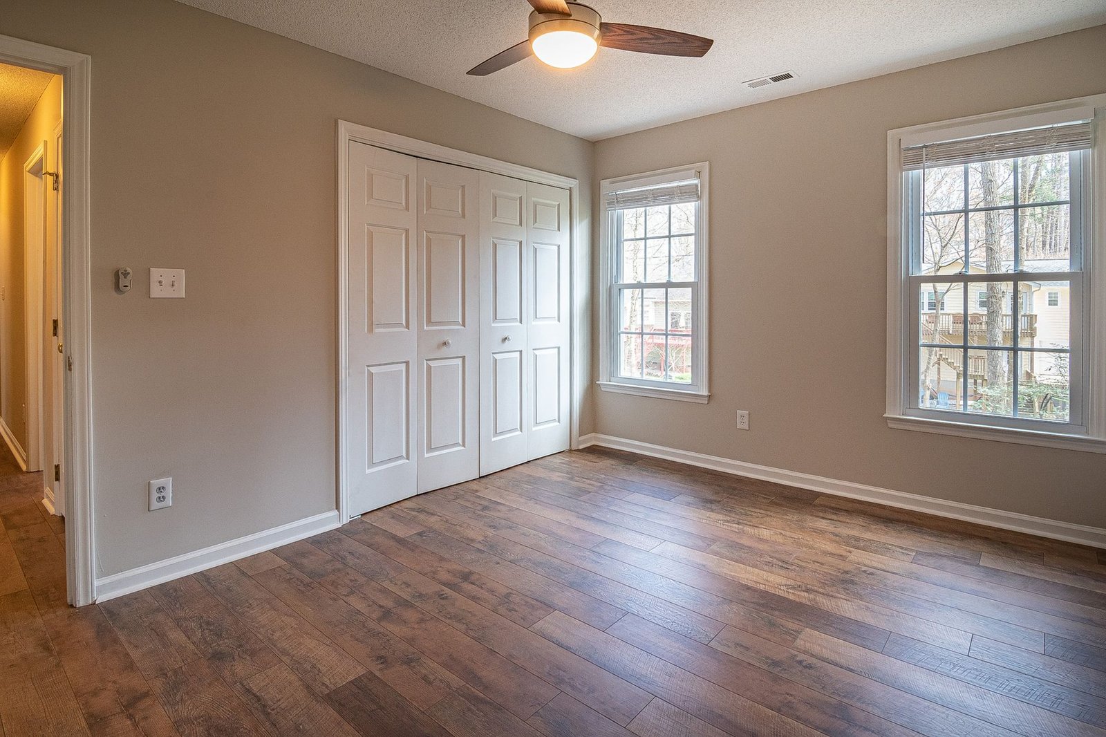 Empty bedroom with a dark plank wood floor, white skirting boards and a ceiling fan