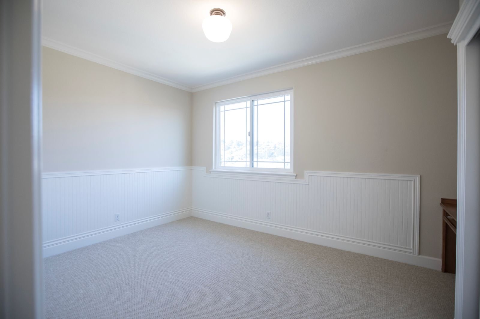 Empty room with a window in the corner, white wainscot panelling and a ceiling light