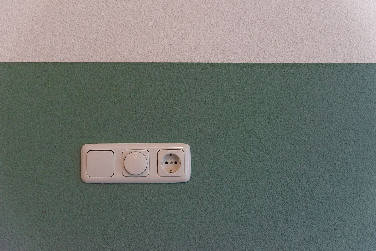 Empty wall socket and switch on a green wall, the socket to inspect for scorch marks once a dehumidifier is unplugged