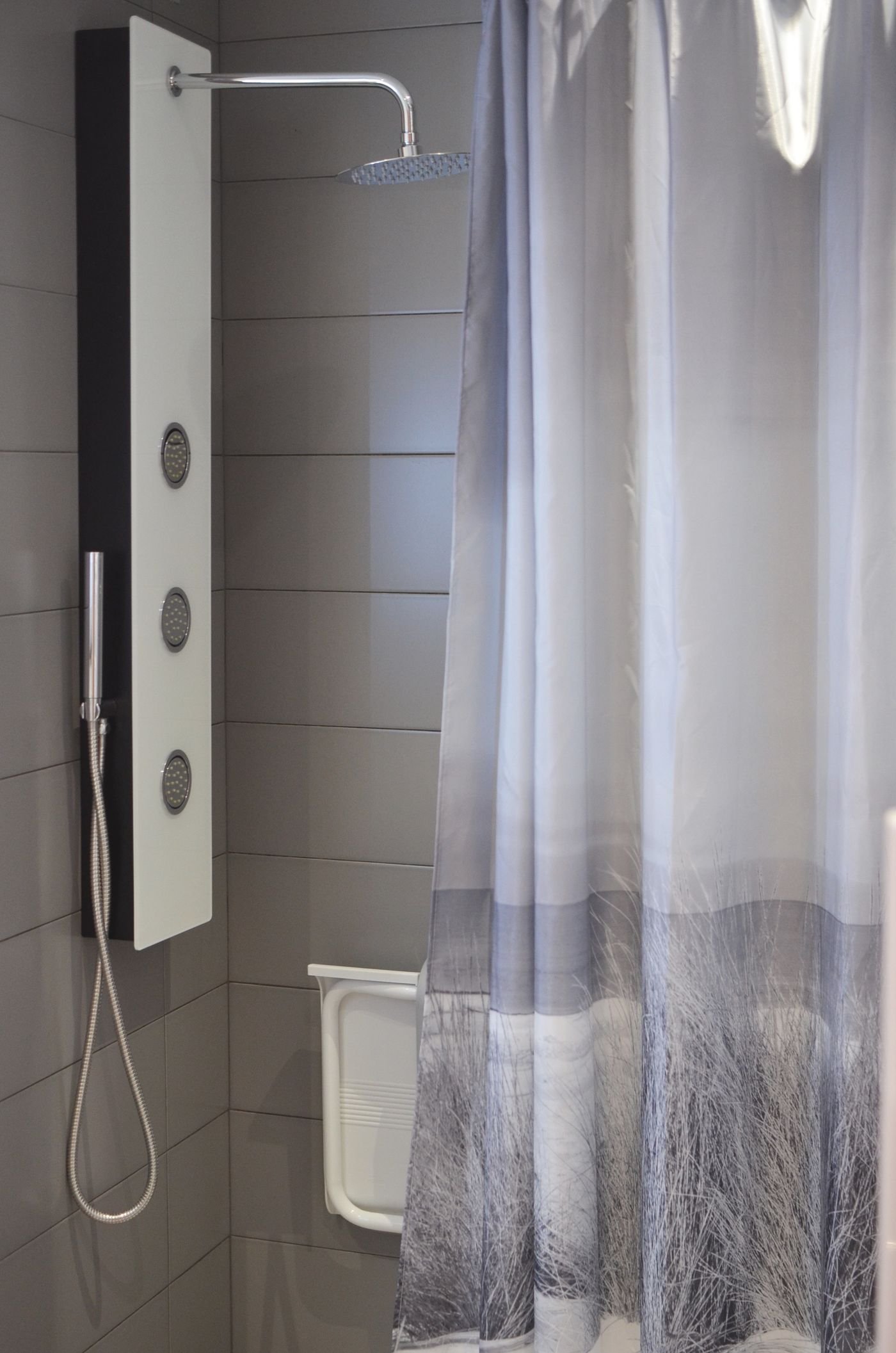 Grey fabric shower curtain hanging straight beside a grey-tiled shower wall