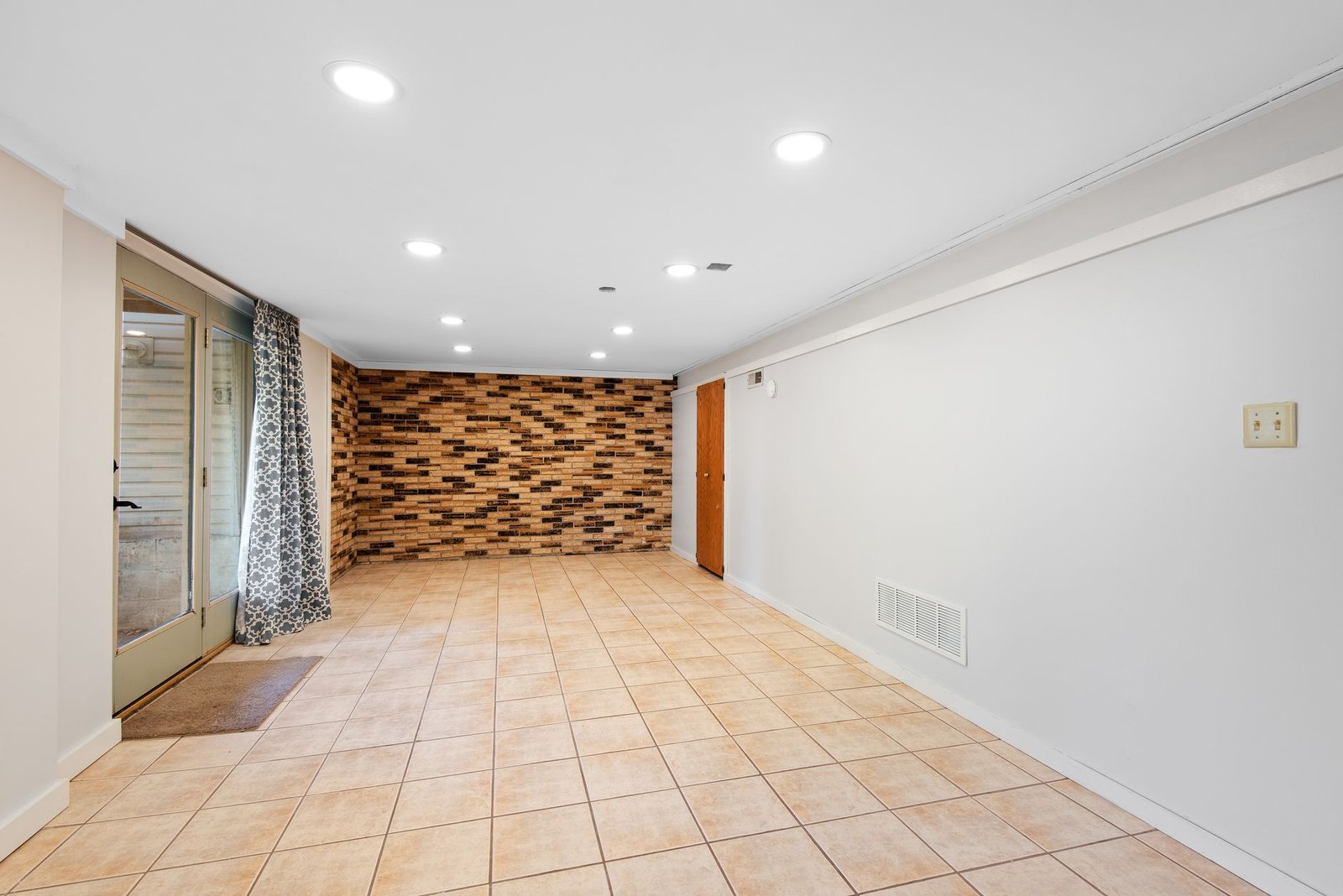 Finished basement with a tiled floor, brick feature wall and a walk-out door, a space that can still run damp