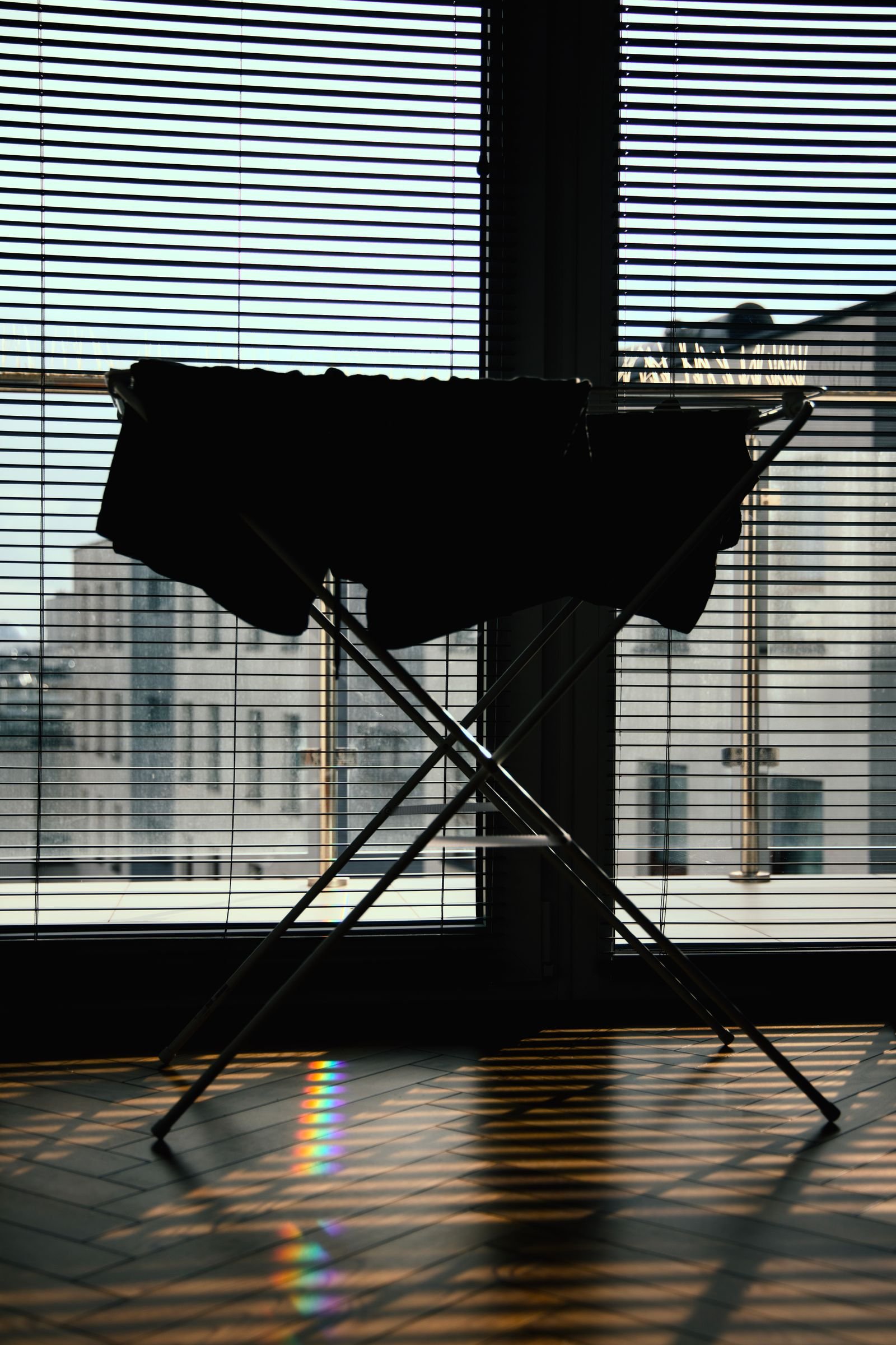 Silhouette of a freestanding X-frame clothes airer with washing, standing by a blinded window