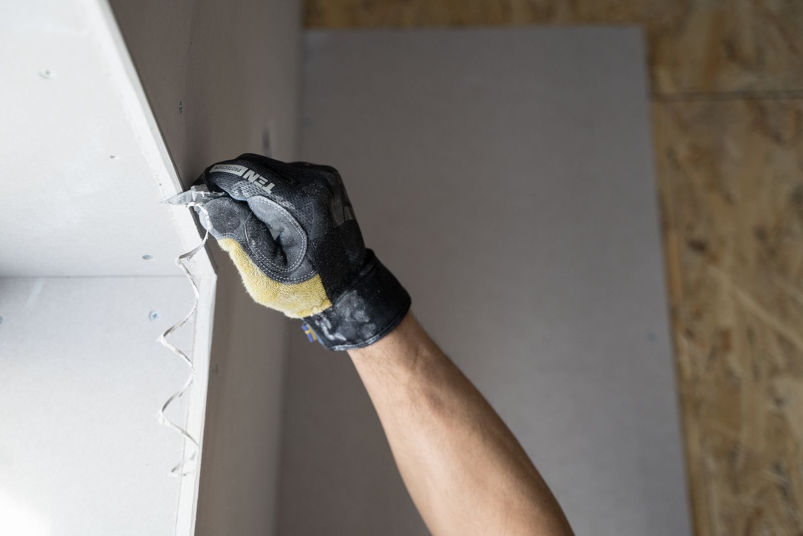 Gloved hand trimming the edge of a plasterboard sheet with a knife during a wall repair