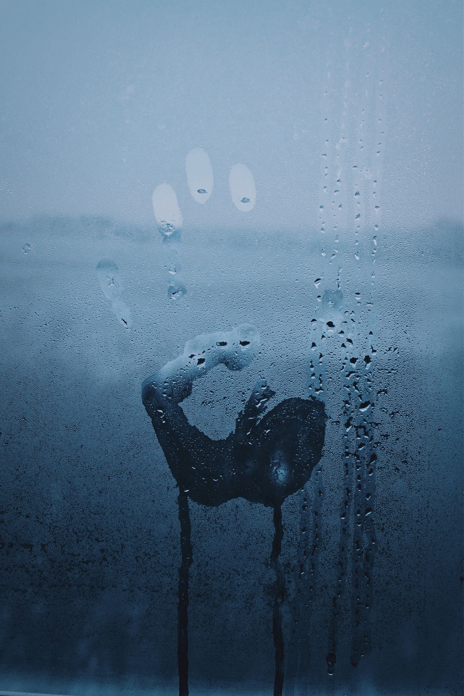 Handprint wiped through heavy condensation on a window pane, with droplets running down the glass
