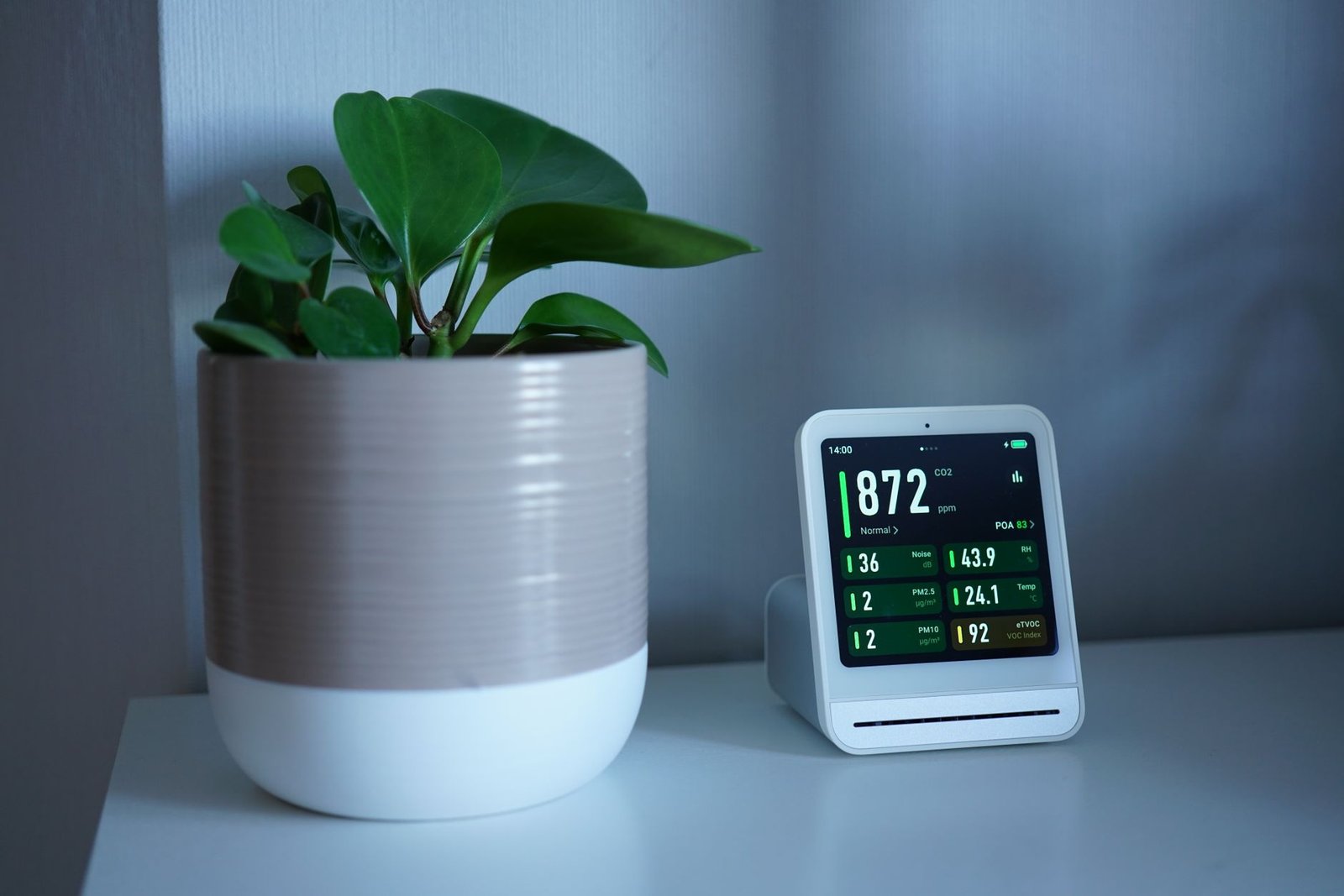 Indoor air monitor on a shelf beside a plant showing relative humidity of 43.9 percent, within the 30-50 percent range
