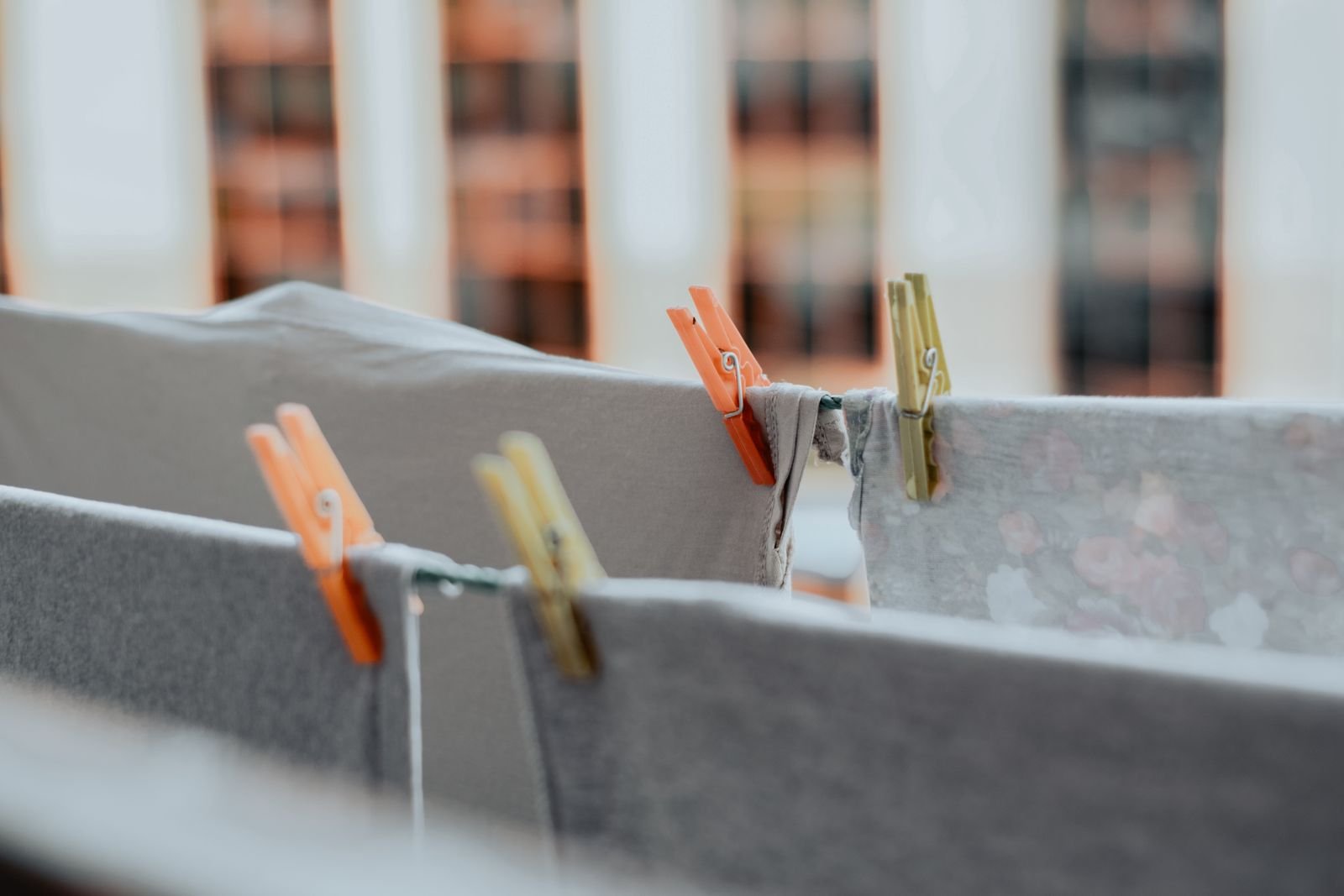 Grey and patterned garments pegged close together on a drying line, with a blurred window view behind