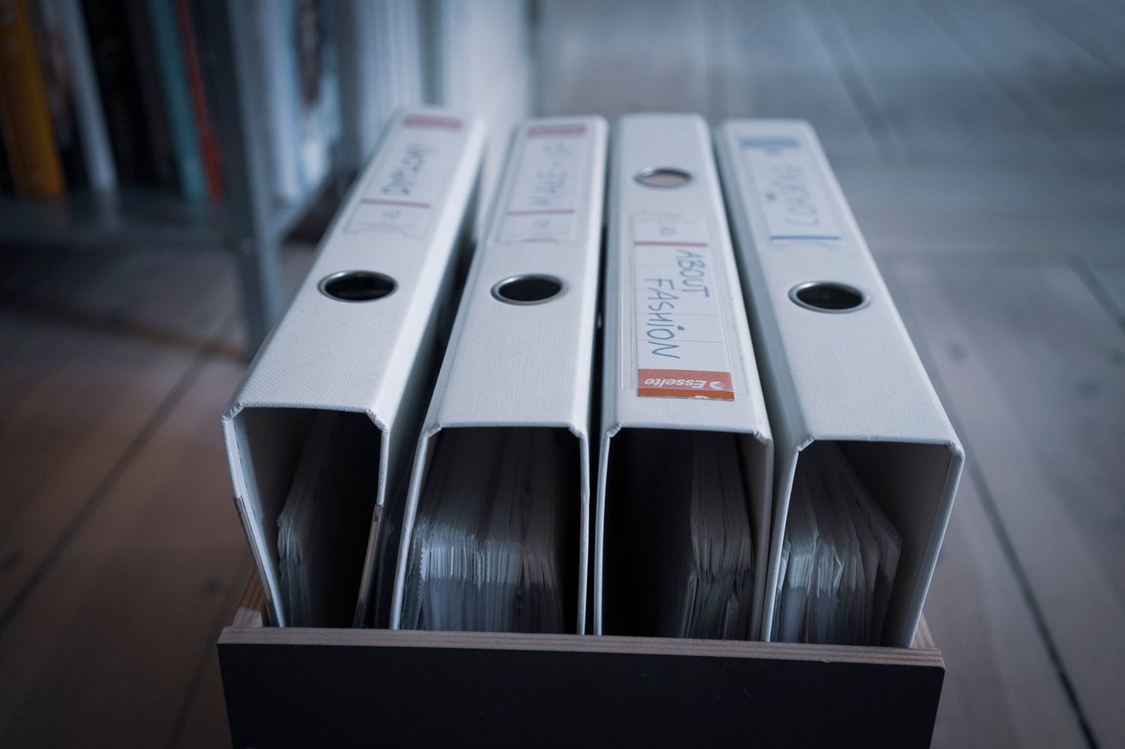 Four lever arch files standing in a wooden box, a dry document store where silica gel sachets are often tucked in