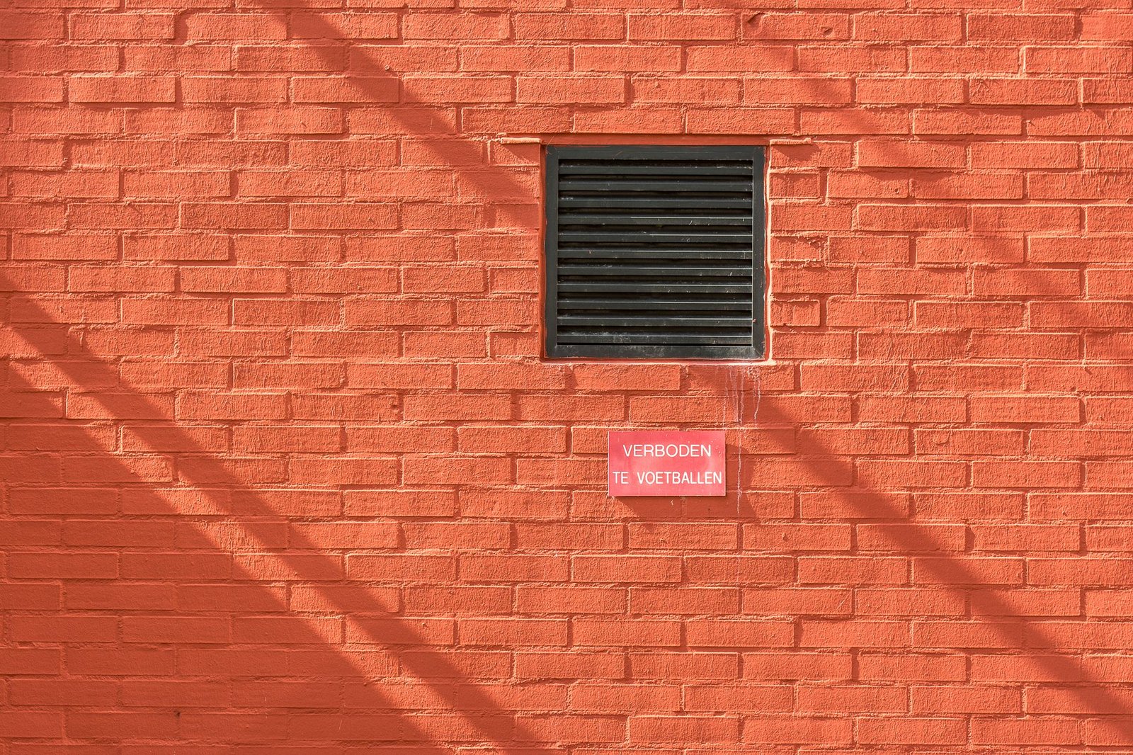 Black louvred vent grille set into a red brick wall, the kind of outside opening an extractor fan duct ends at