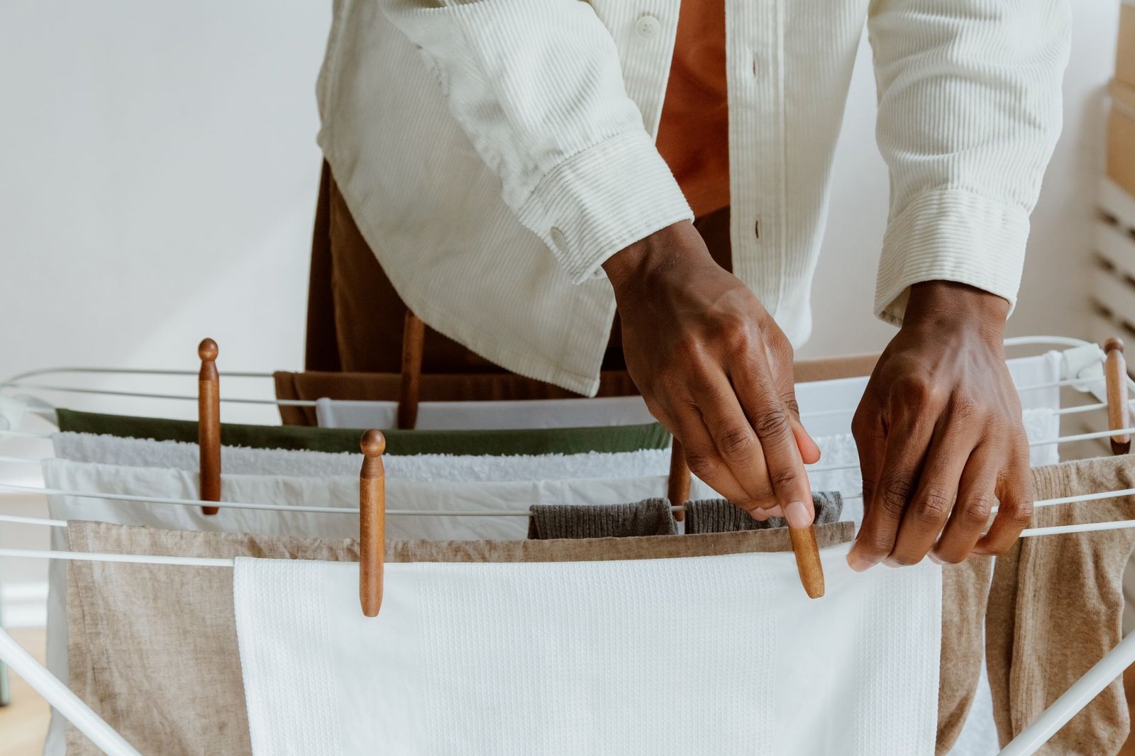 Man hanging washing on a white indoor clothes airer, the setup a dehumidifier turns into a drying room