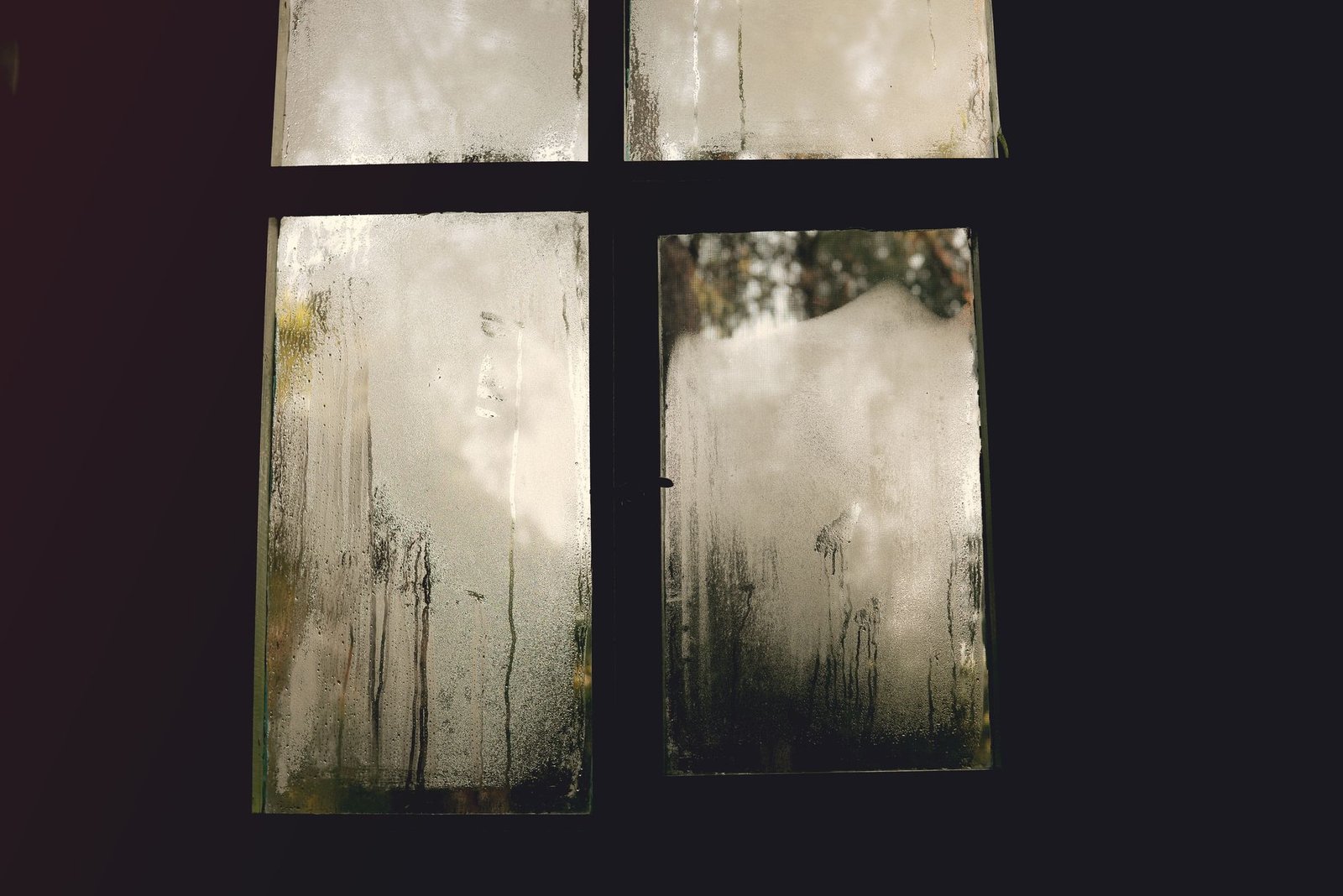 Multi-pane window with condensation and running droplets covering the glass in low light
