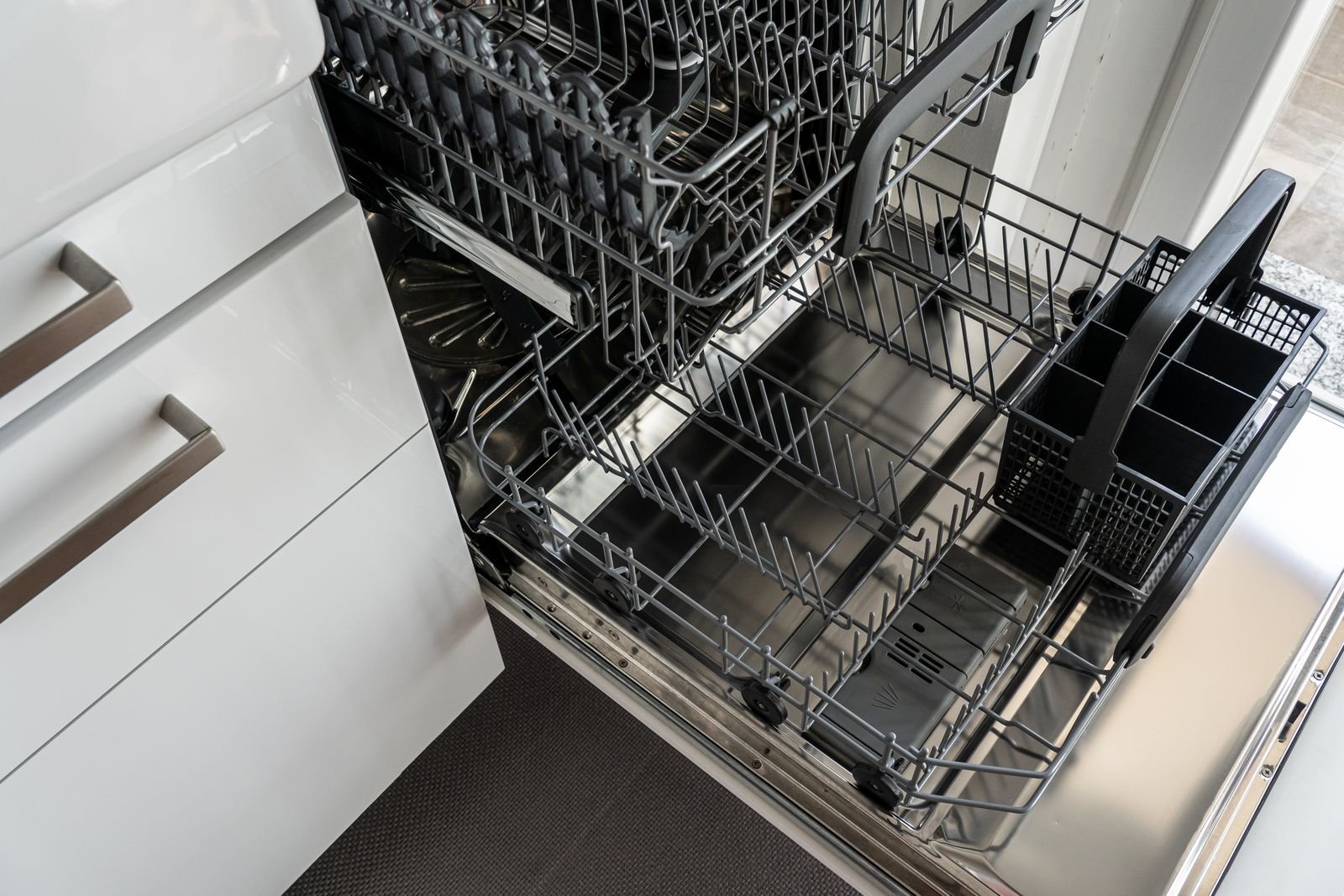 Open built-in dishwasher with empty racks in a white kitchen