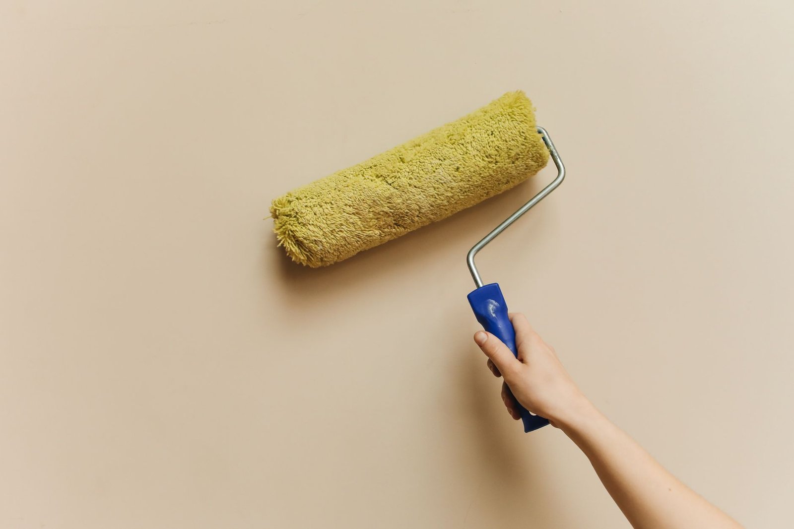 Hand rolling paint onto a plain beige wall with a yellow roller