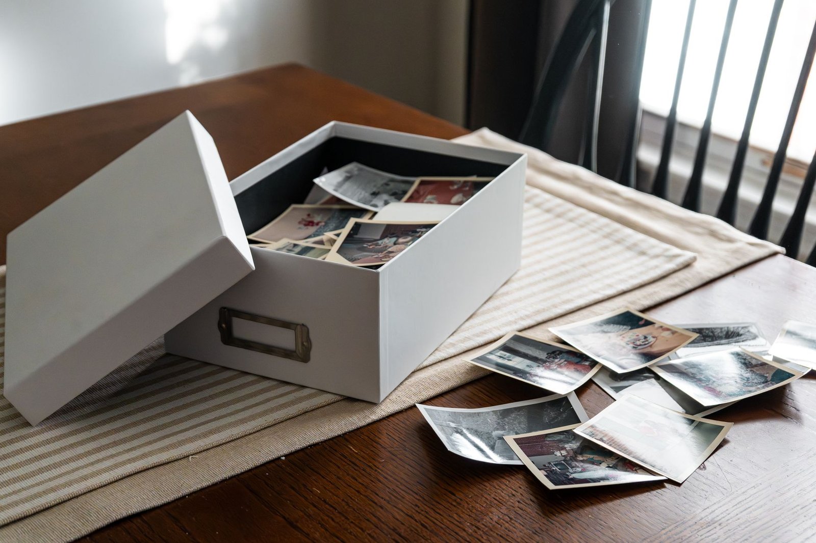 White lidded box of colour photo prints on a wooden table with more prints beside it