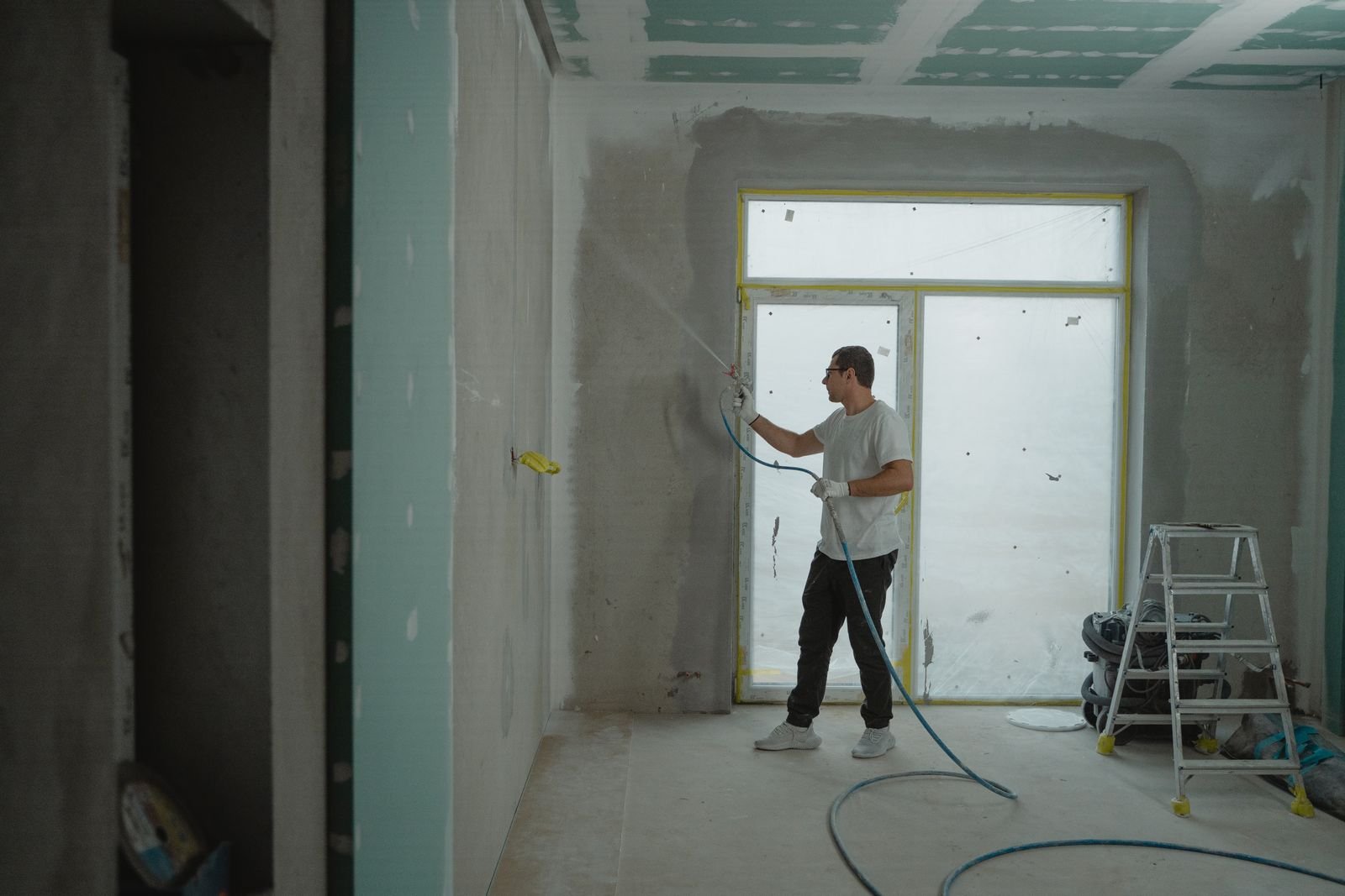 Room under renovation with plasterboard lining the walls and a worker painting, where replacement board goes in after the damp is fixed