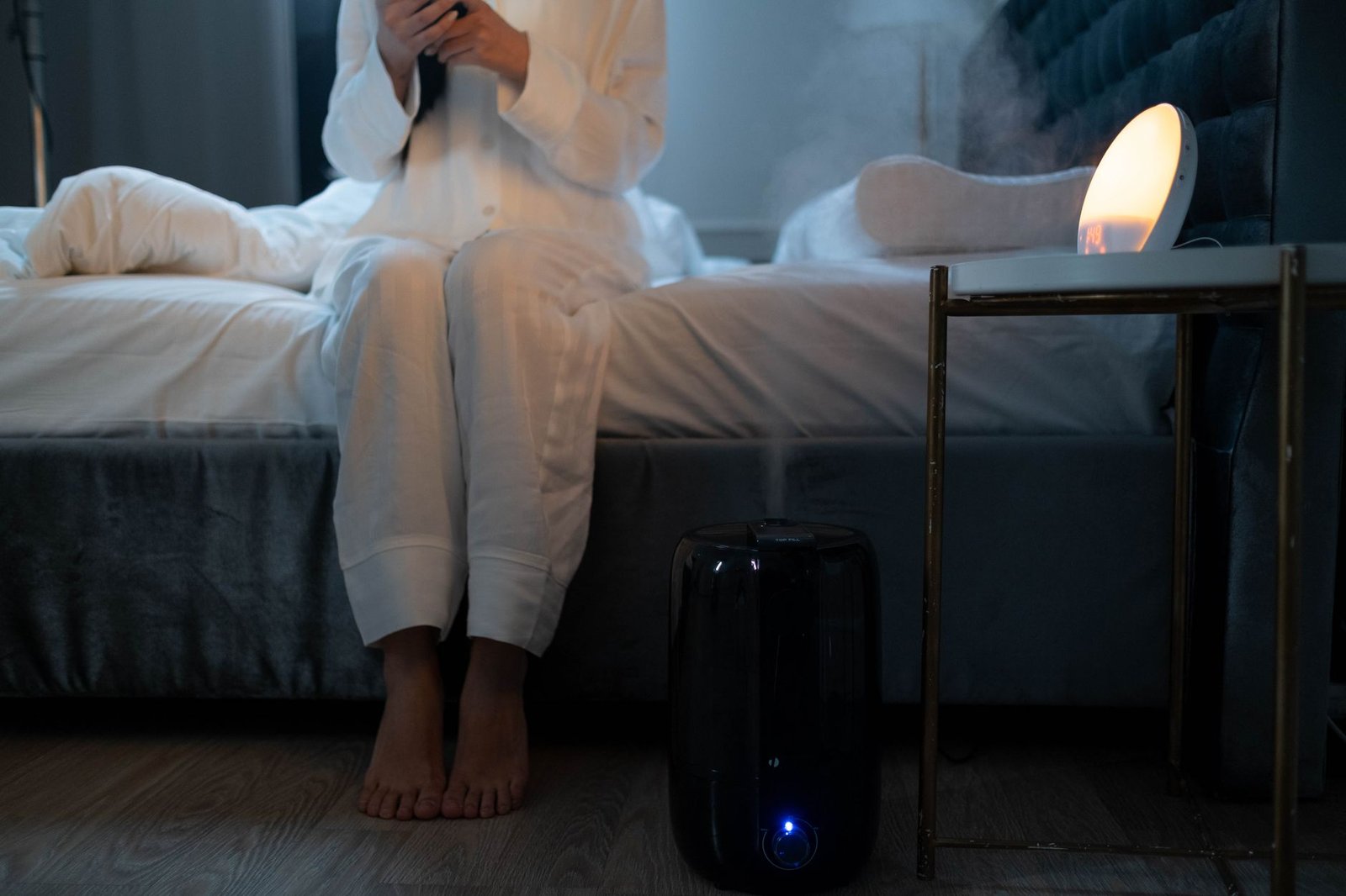 Portable humidifier releasing mist beside a bed in a dim bedroom