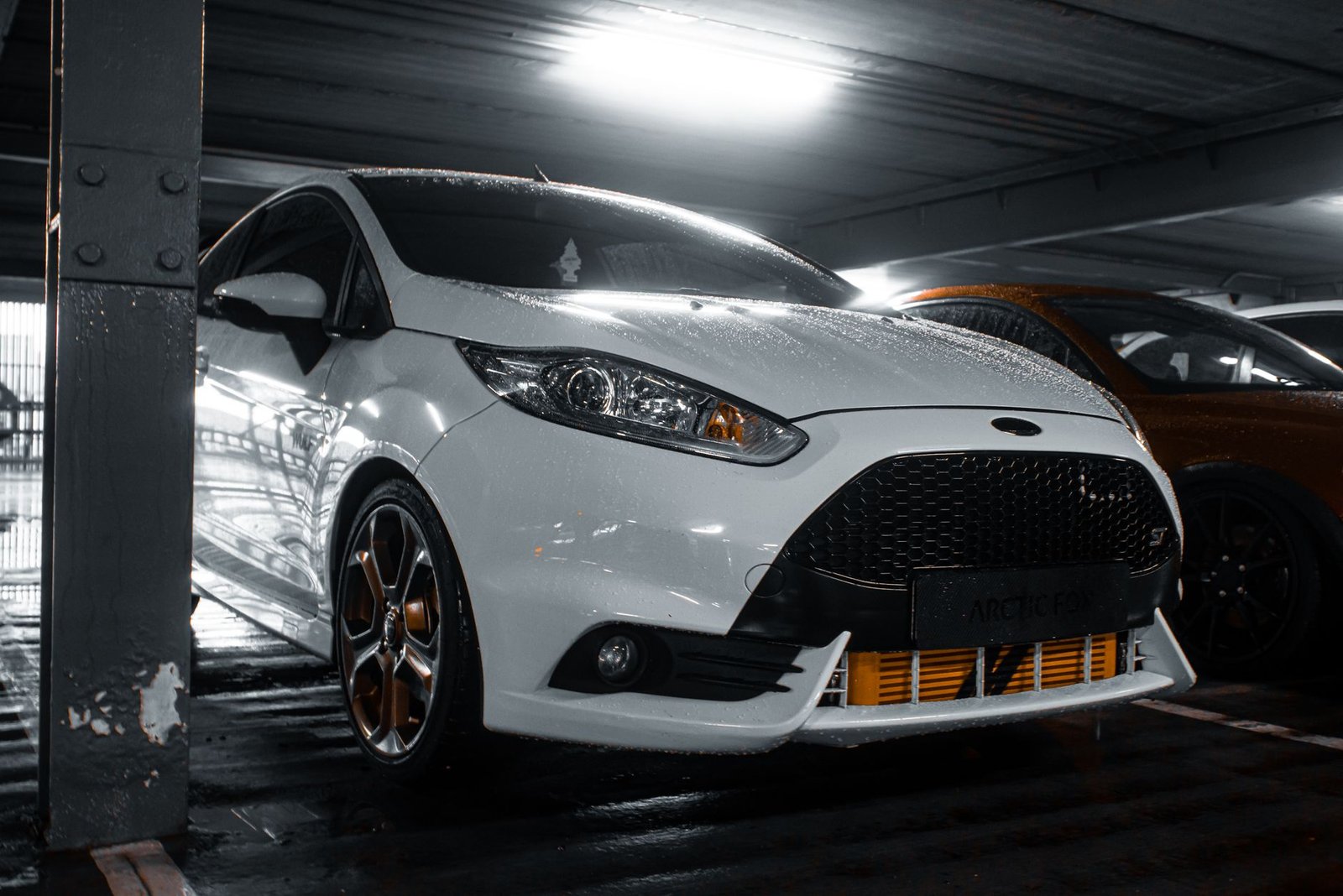 White car beaded with rainwater parked under cover, the kind of load a wet car carries into a garage