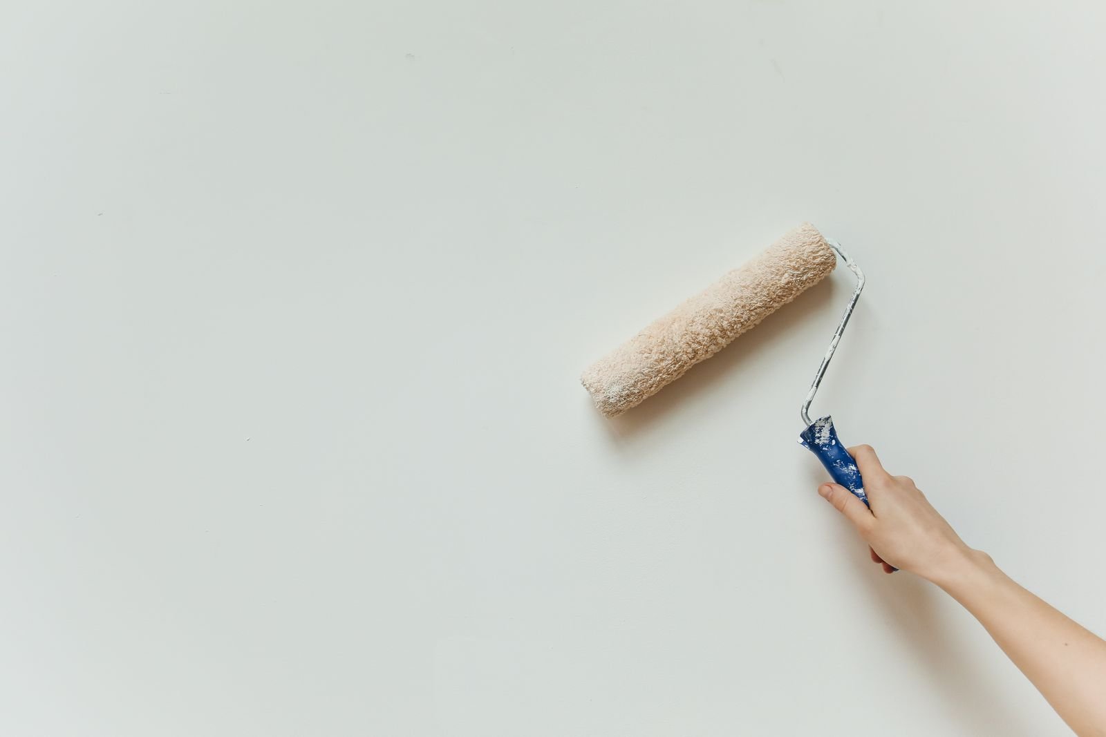 Hand rolling fresh paint onto a pale wall