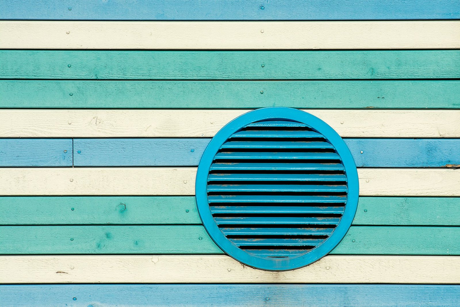 Round blue louvre vent set into a wall of blue, green and cream painted timber boards