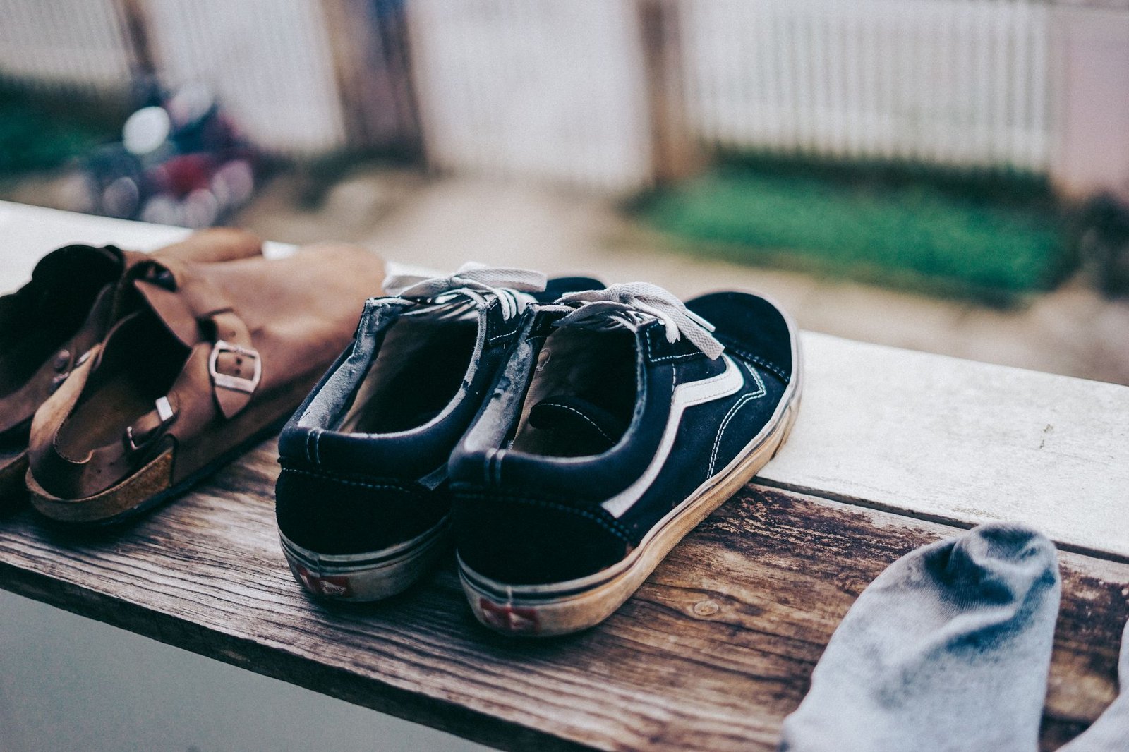 Navy canvas shoes and brown leather sandals airing on a wooden ledge outdoors