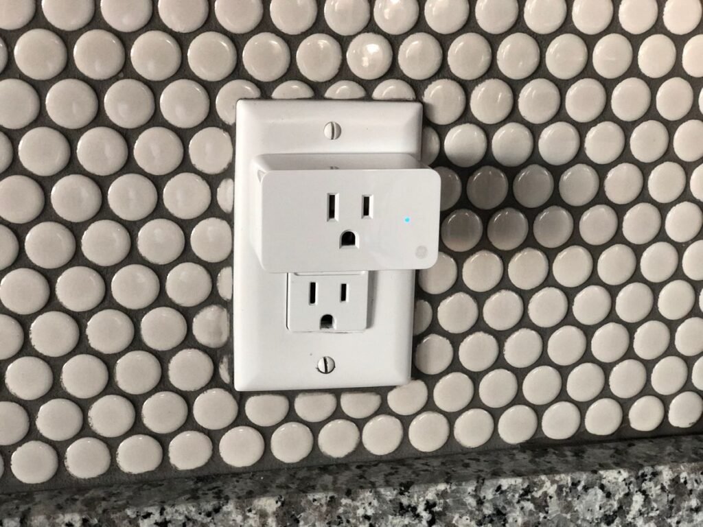 White smart plug fitted into a wall socket with a small blue status light