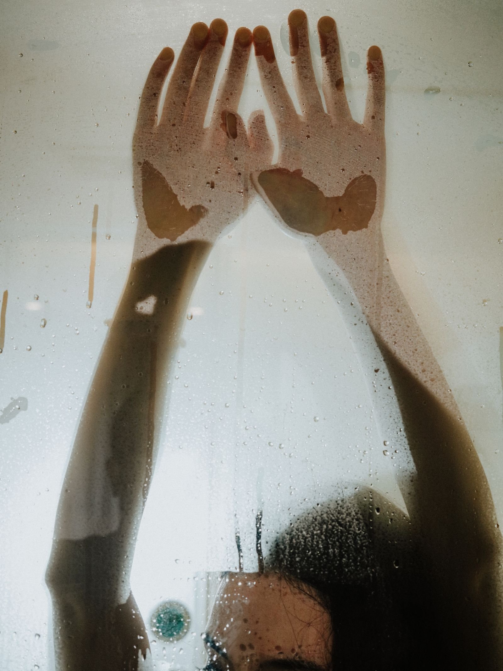 Hands pressed against a steamed-up shower screen covered in condensation droplets