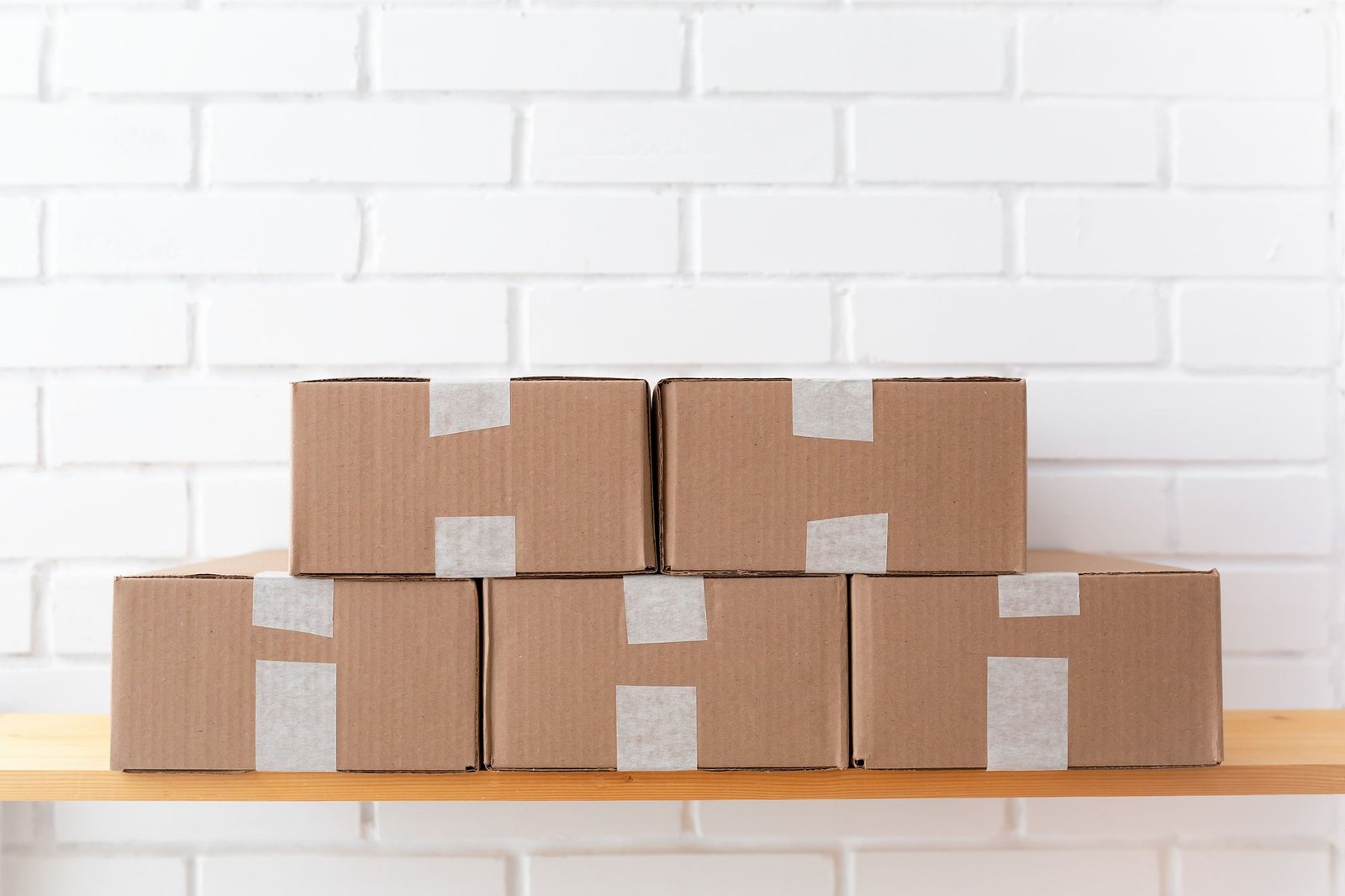 Taped cardboard boxes stacked on a shelf against a white brick wall, the kind of stored cardboard that can hold damp and smell musty