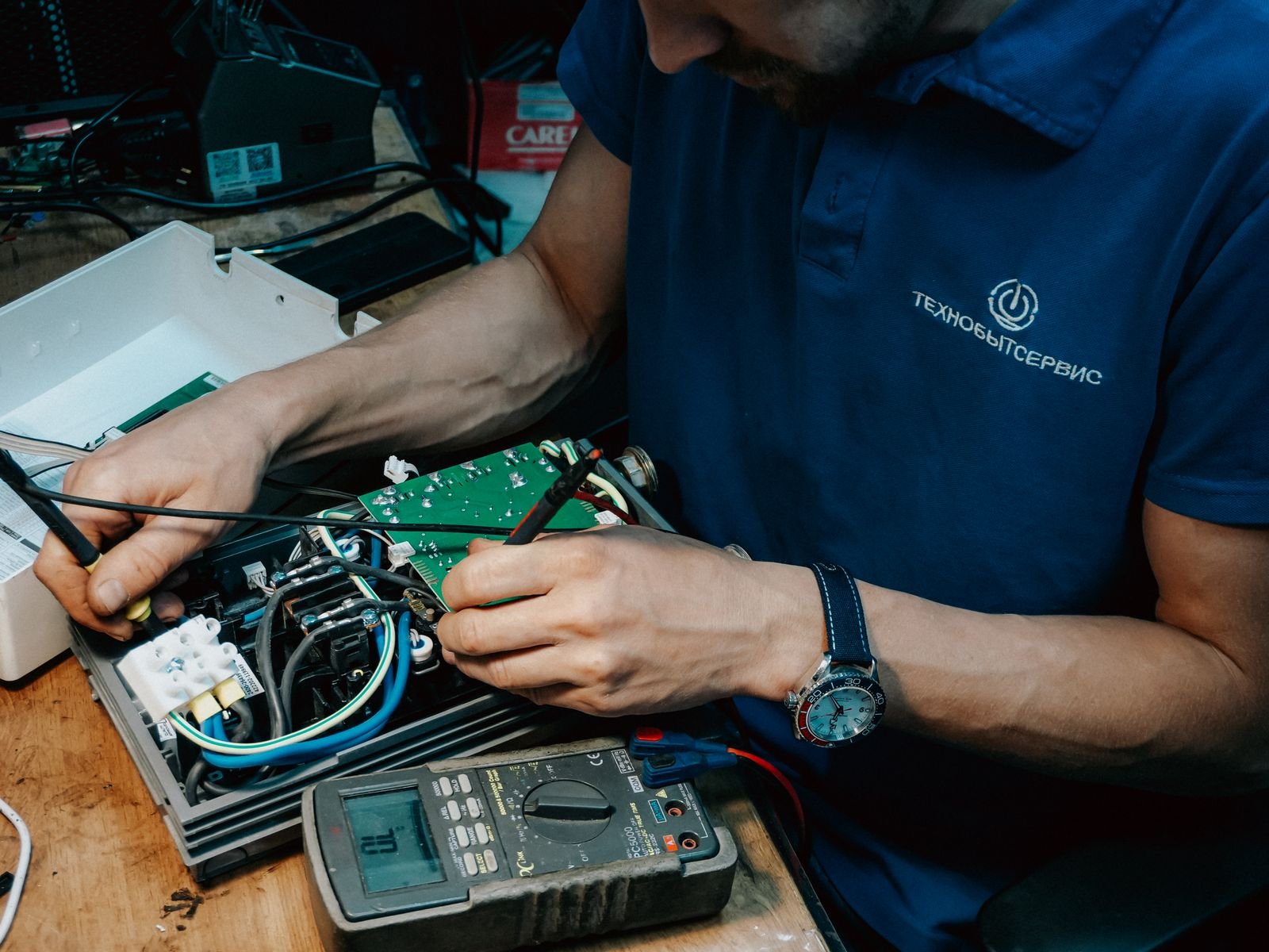Technician testing an appliance circuit board with a multimeter and a screwdriver in a workshop