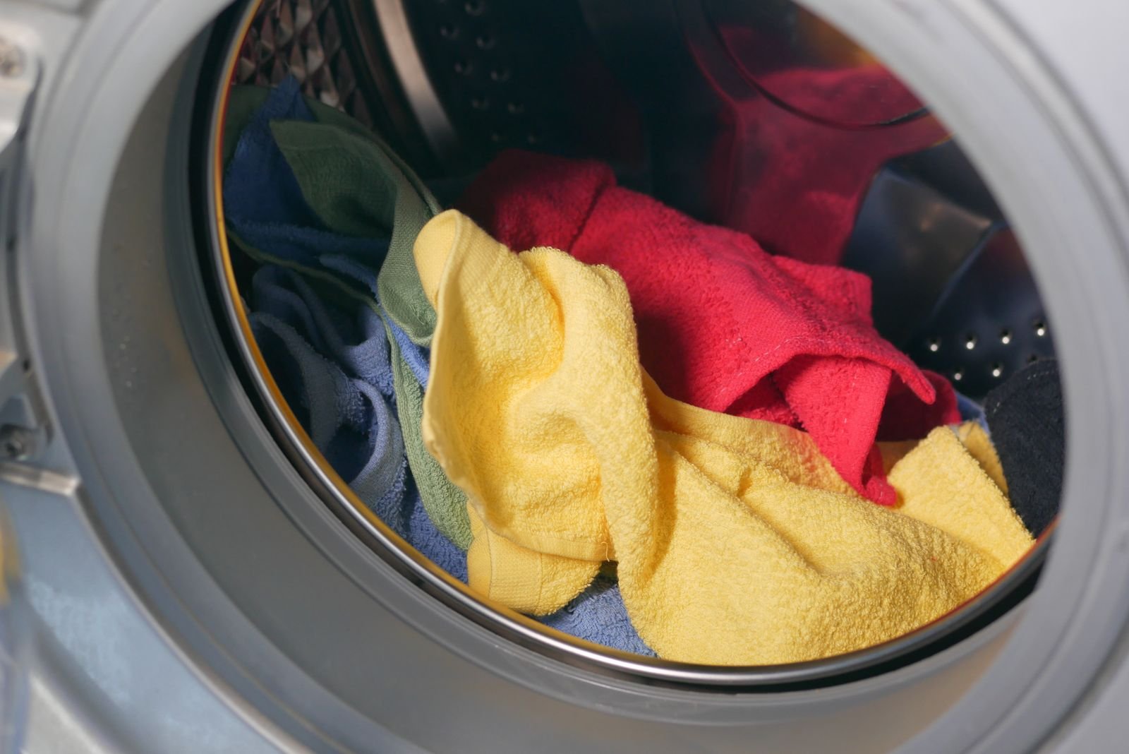 Colourful towels piled inside the drum of a front loading washing machine