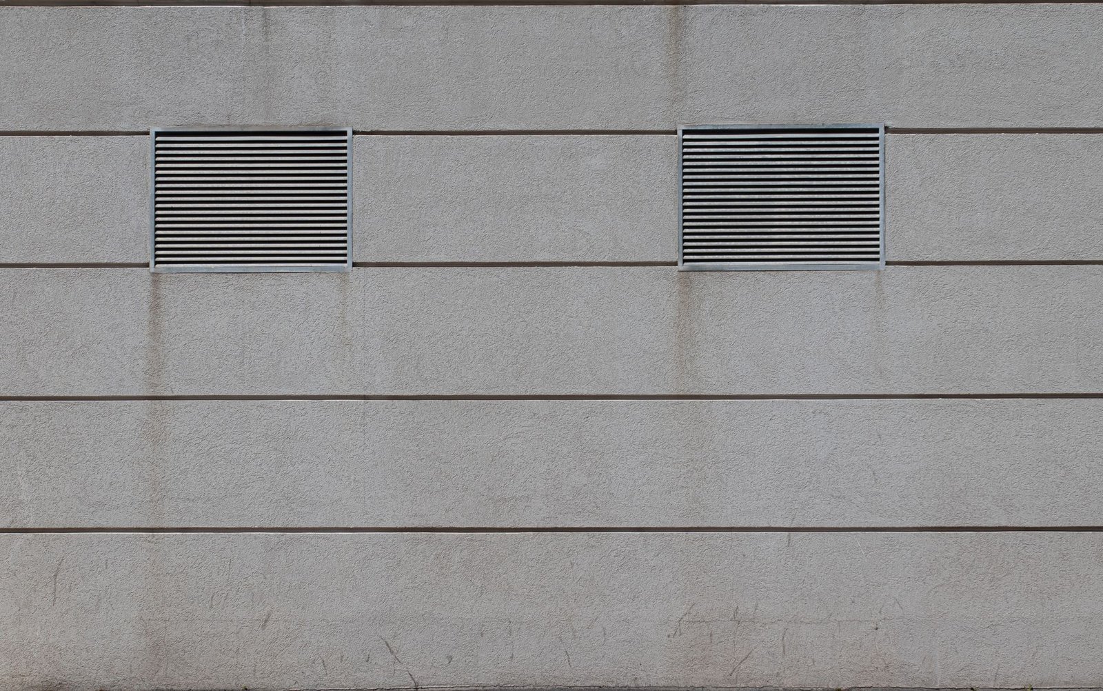 Two rectangular louvred air vents set into a plain grey rendered wall