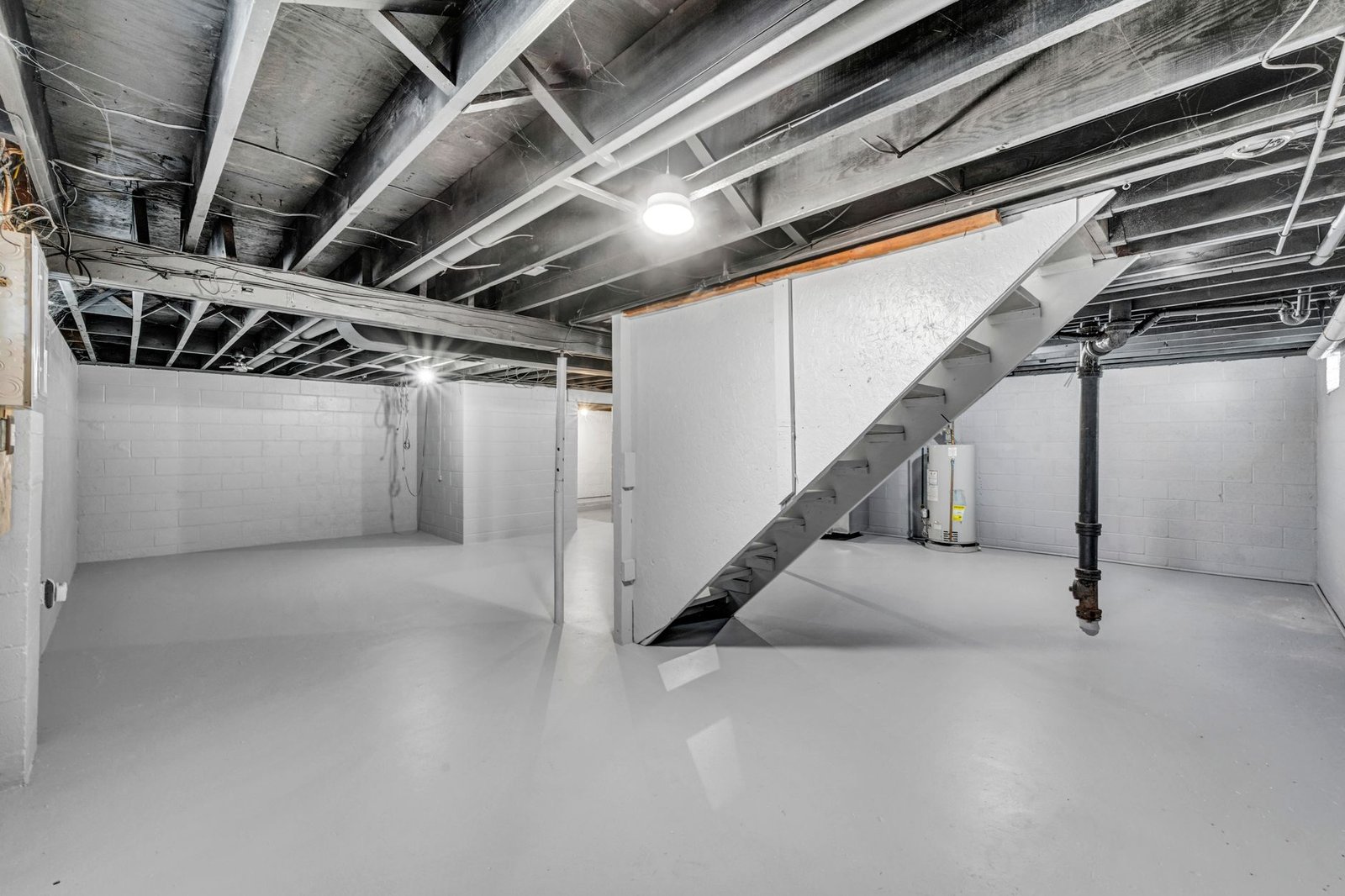 Unfinished basement with a water heater, a drain pipe and exposed joists, where cold pipes often sweat