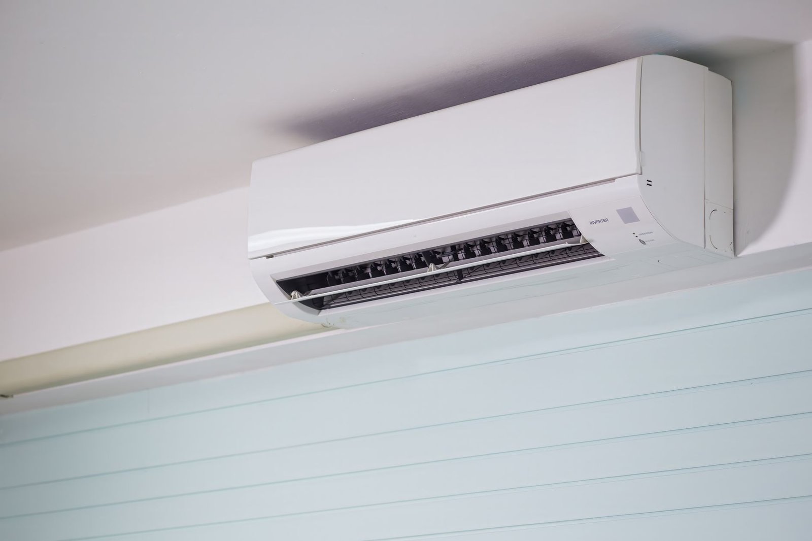 White wall-mounted split air conditioner indoor unit fixed high on a wall below the ceiling