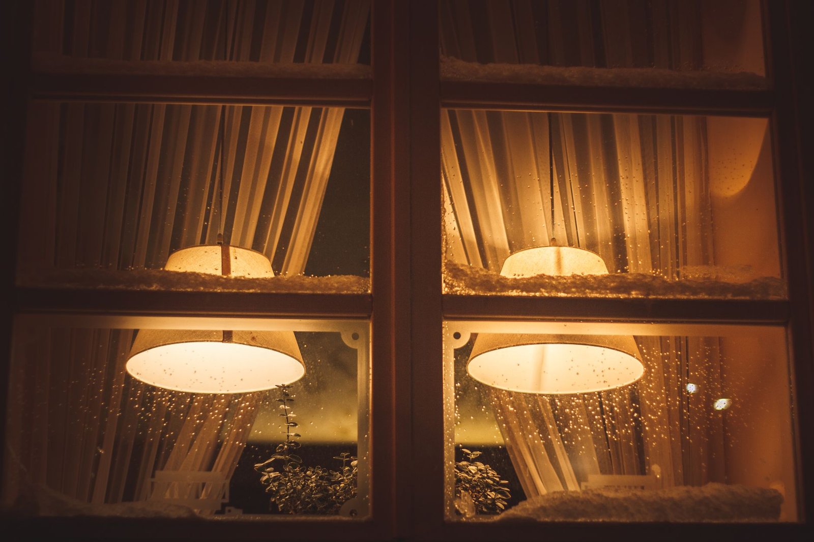Warm lit windows of a house on a snowy winter night with snow on the sills and water droplets on the glass