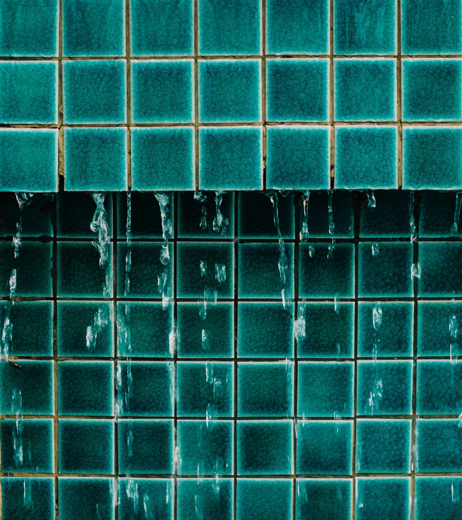Water running down a wall of teal glazed tiles, showing how water reaches the joints between tiles