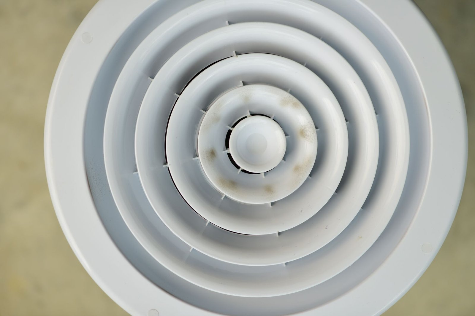 Round white ceiling vent grille with brown dust marks on the inner discs
