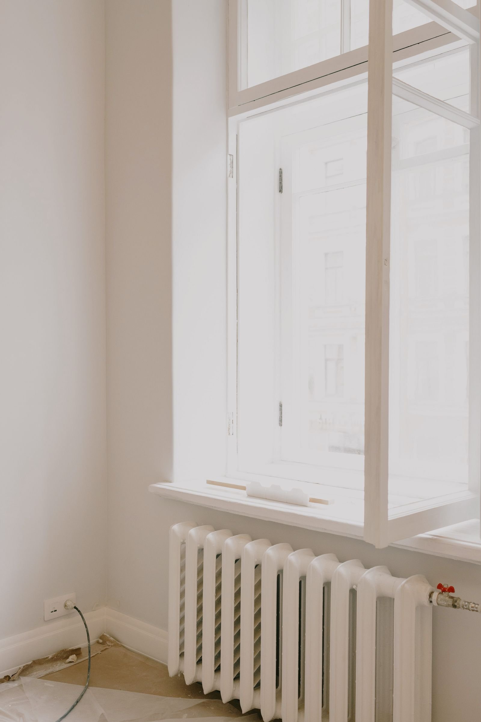 White cast-iron radiator under an open window in a bare room with white walls