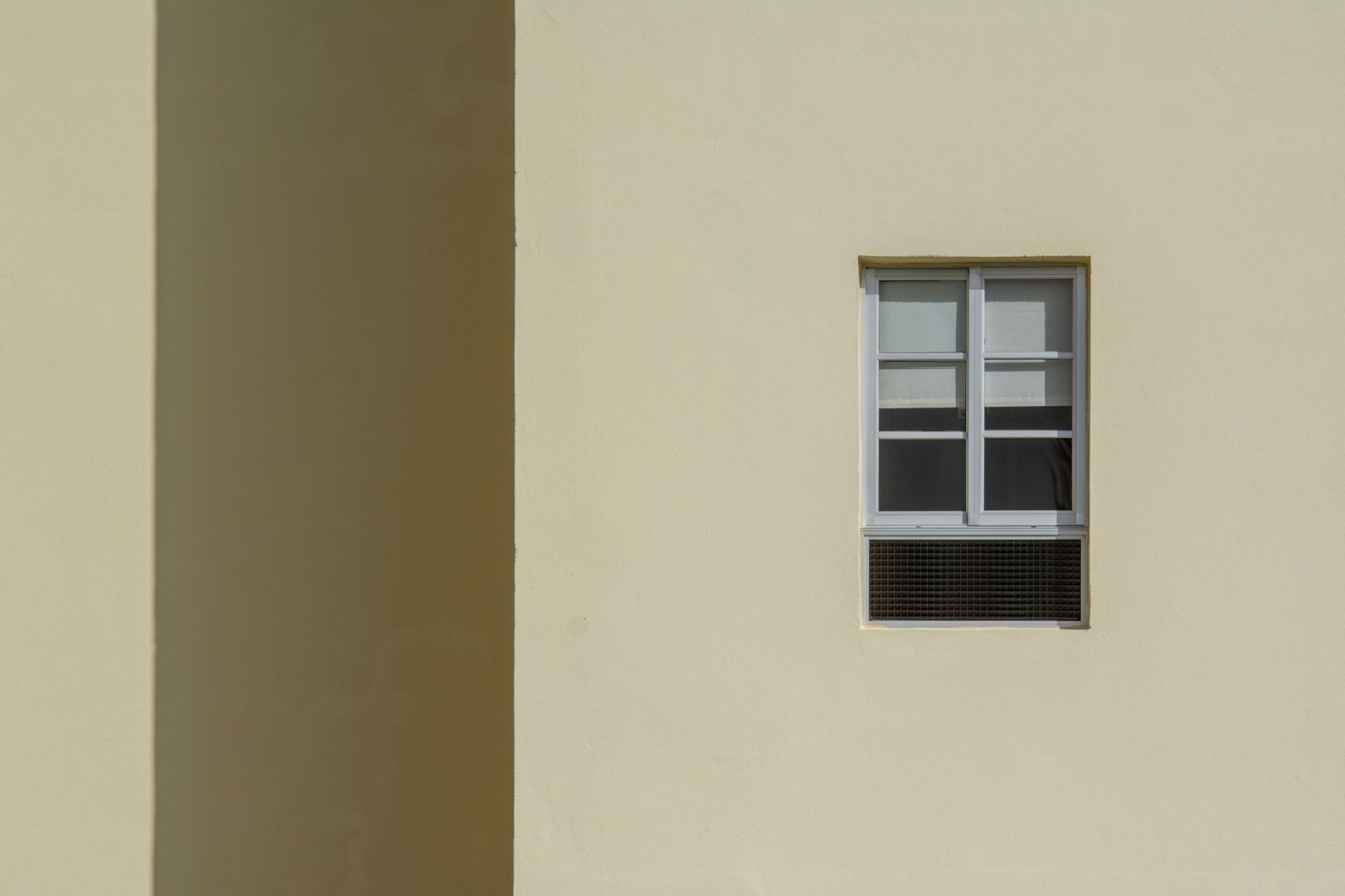 A small window in a cream wall with a ventilation grille set into the wall below it