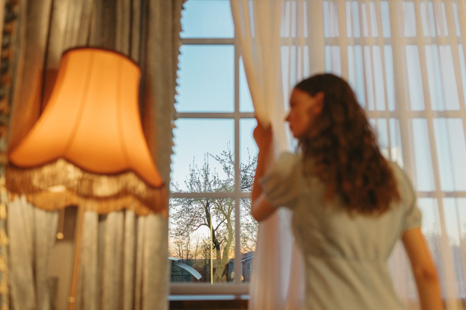 Woman drawing back sheer curtains from a window in the morning to let air reach the glass
