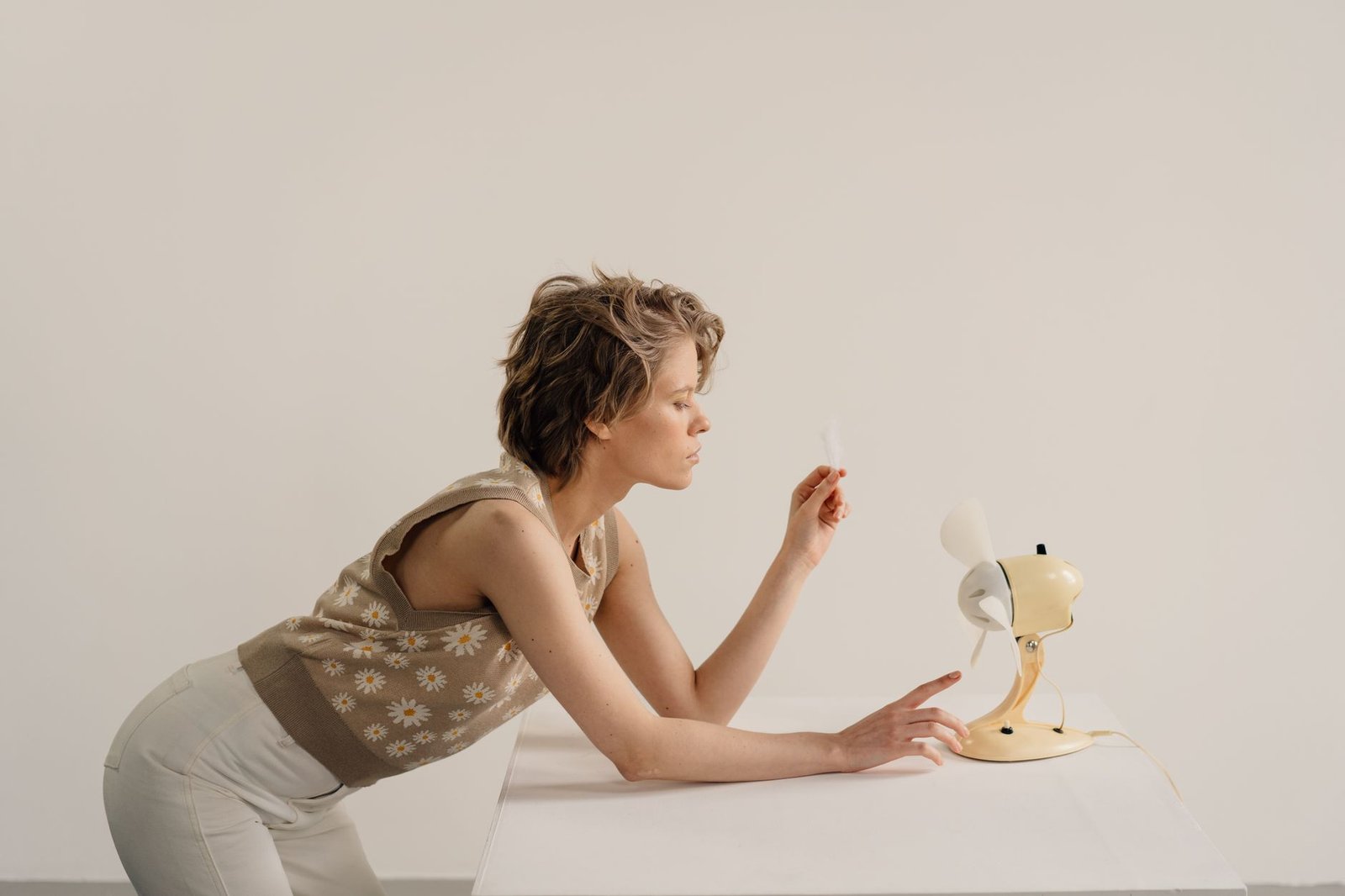Woman holding a feather in the airflow of a small desk fan to feel the moving air